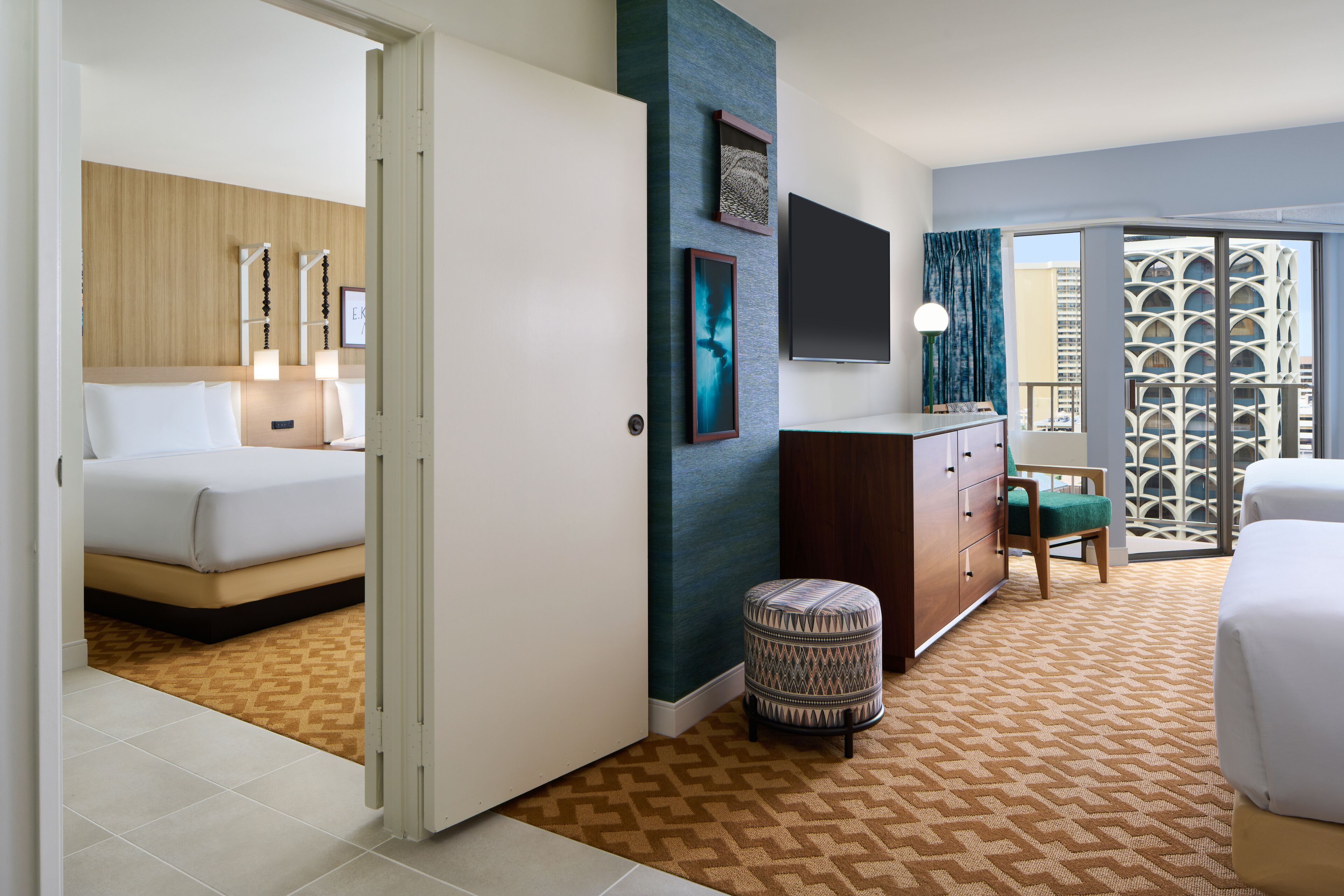A hotel room with a bed, a desk, a chair, and a view of a building through a window.