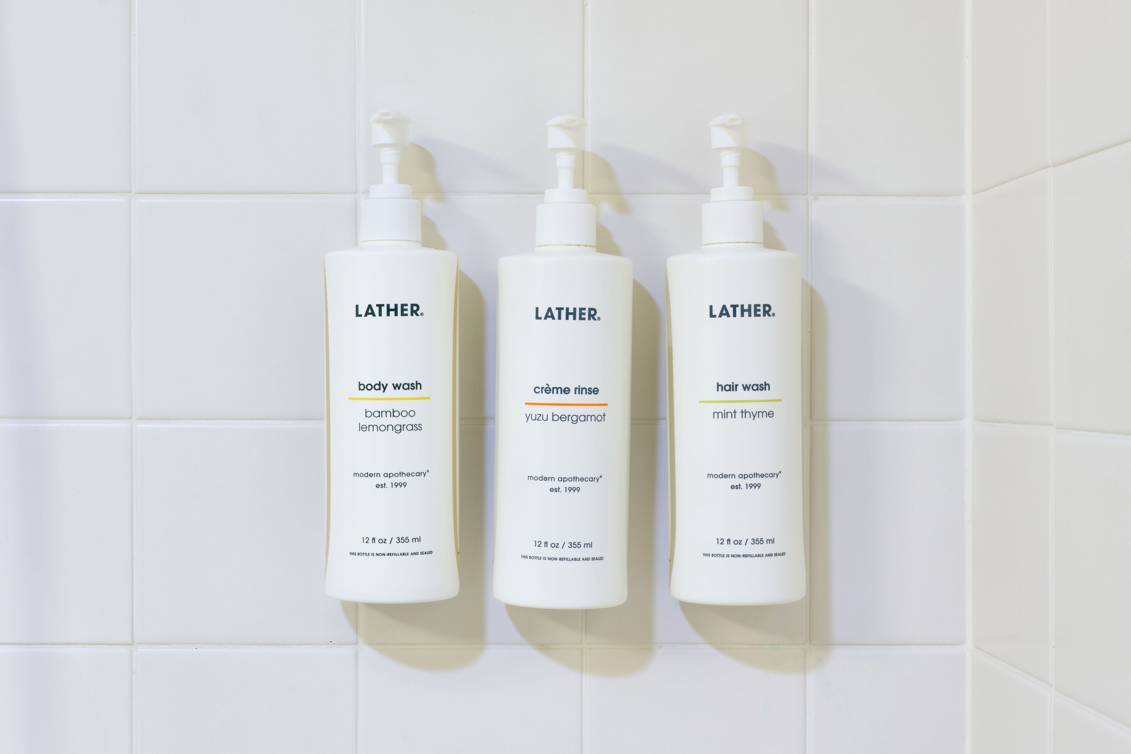 Three Lather body wash bottles on a tiled wall.