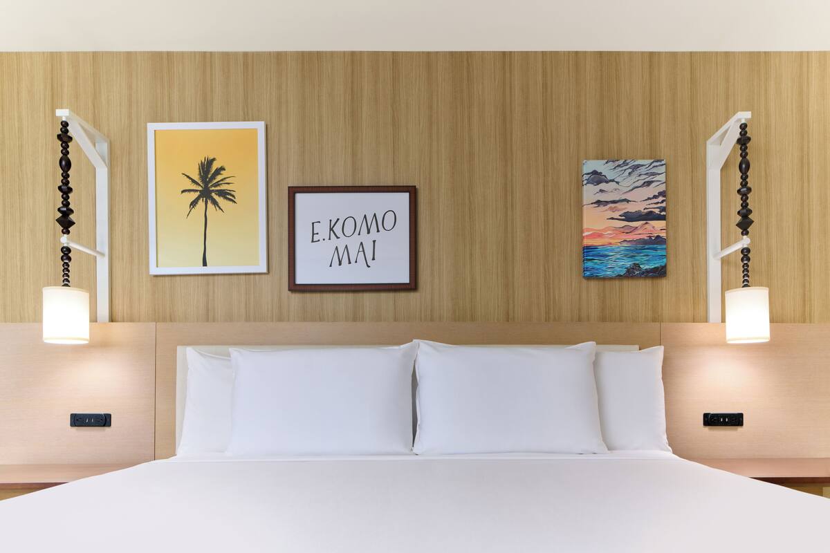A hotel room with a bed, two wall-mounted lamps, and three framed pictures on the wall.