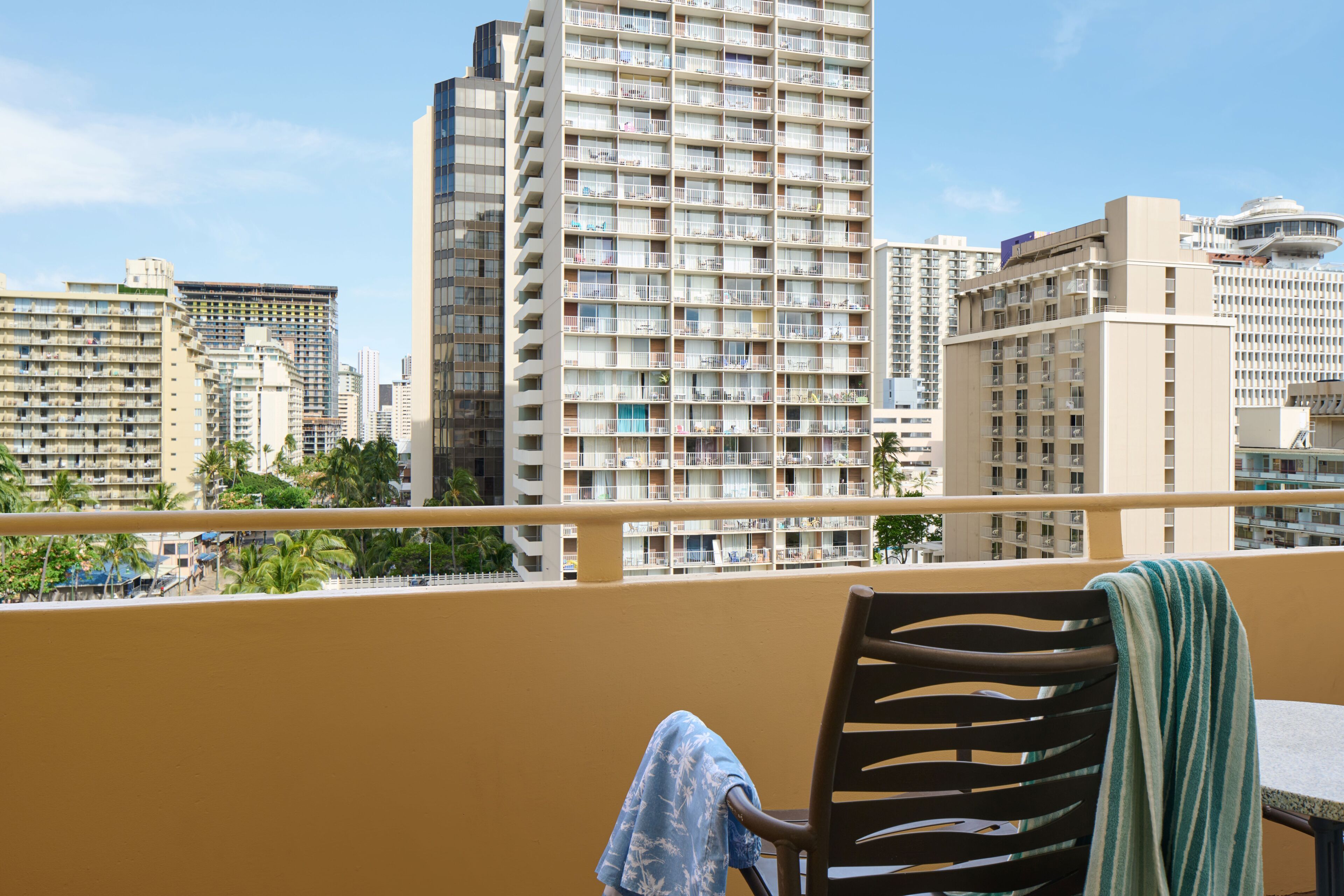 A balcony with a view of high-rise buildings, a chair with a towel, and a table.