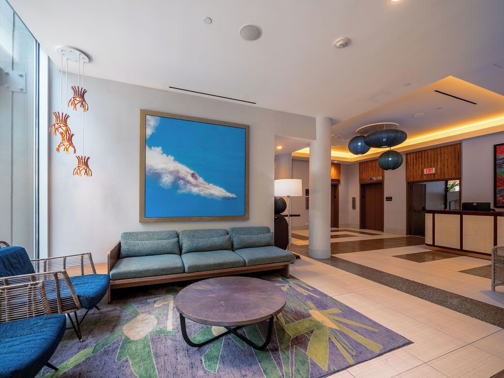 A modern lobby with a sofa, chairs, a round table, and a large painting of clouds.