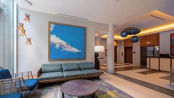 A modern lobby with a sofa, chairs, a round table, and a large painting of clouds.