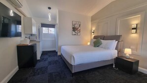 A hotel room with a bed, bedside tables, a desk with a chair, a flat-screen TV, and a window with a view of the outside. - Waterview Gosford Motor Inn (West Gosford)
