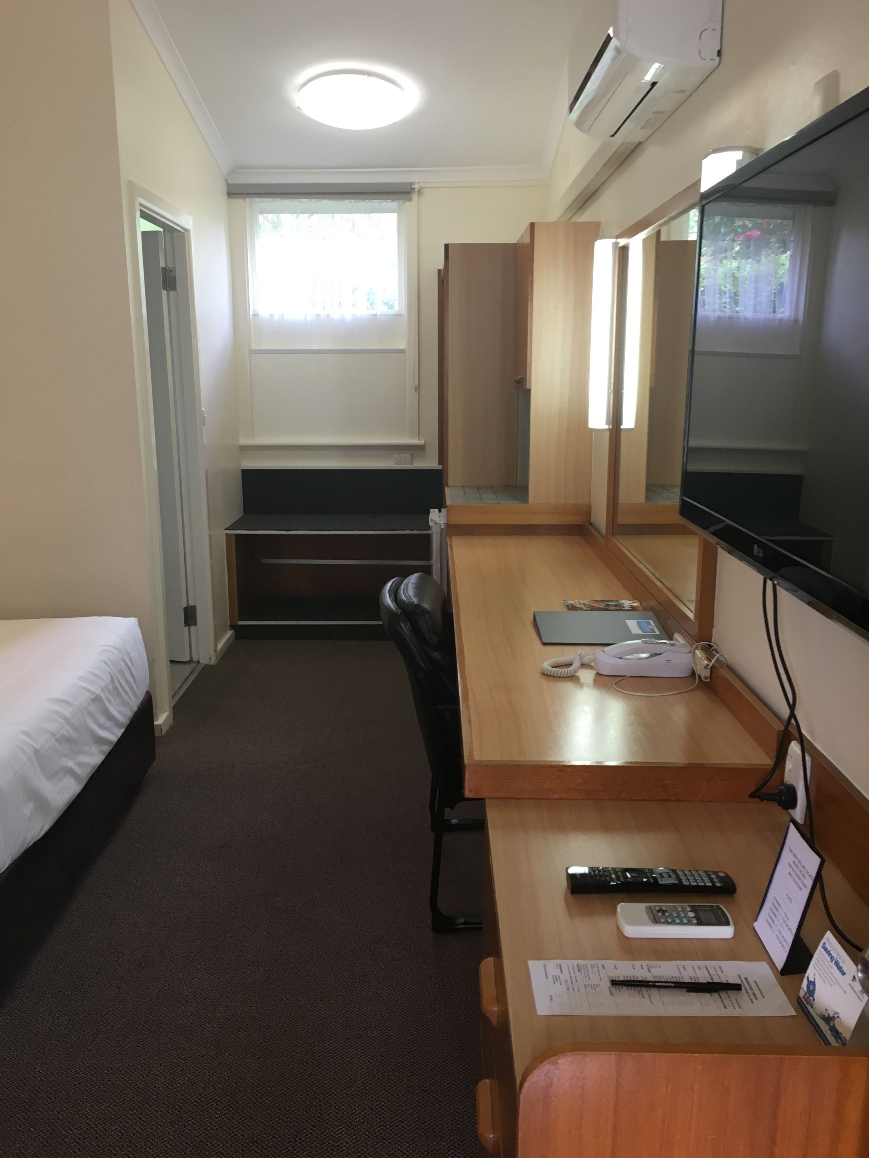 A hotel room with a bed, a desk with a computer, a chair, a TV, and a window with curtains.