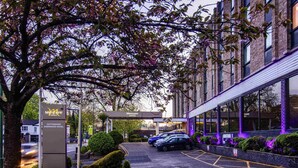 A hotel entrance with a parking area, a tree with pink blossoms, and a building with purple lighting. - Mercure Nottingham Sherwood Hotel (Nottingham)