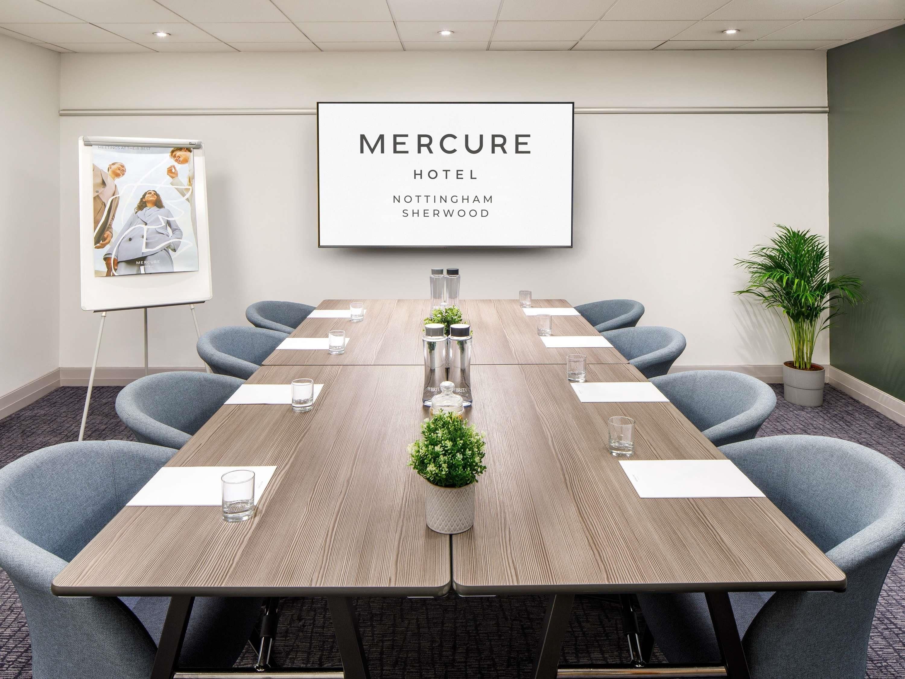 A conference room with a long table, six chairs, a potted plant, and a framed sign on the wall.