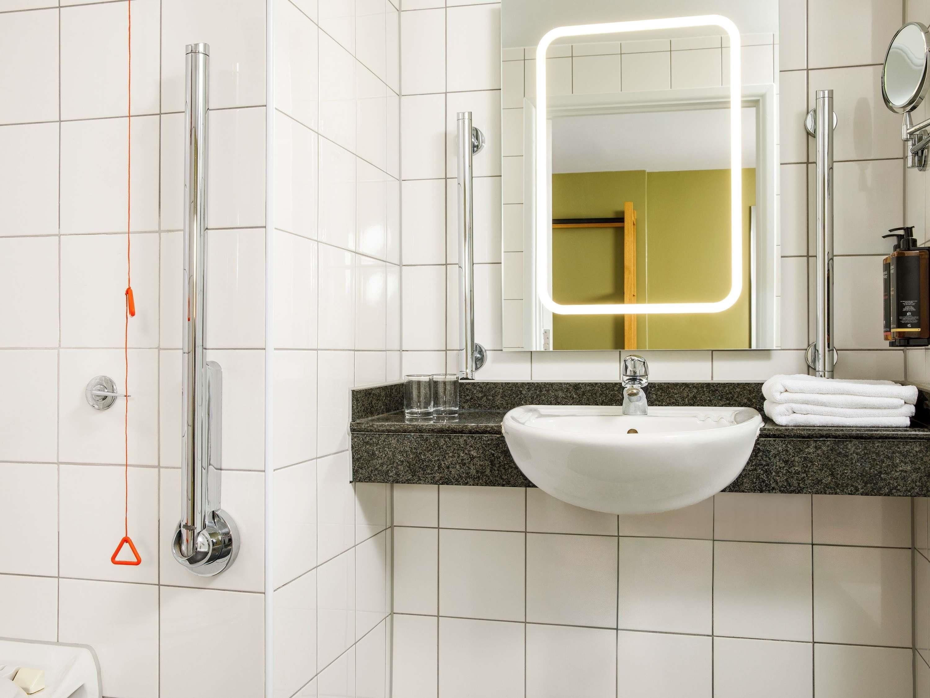 A modern bathroom with a white sink, a mirror with a light, a shower, and a towel rack.