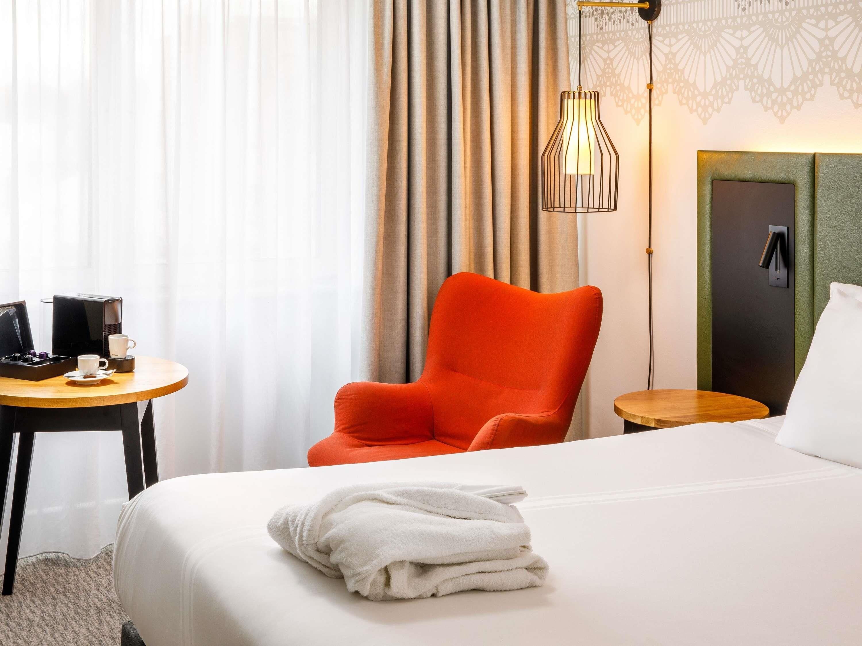 A hotel room with a bed, a chair, a table with a coffee maker, and a lamp.