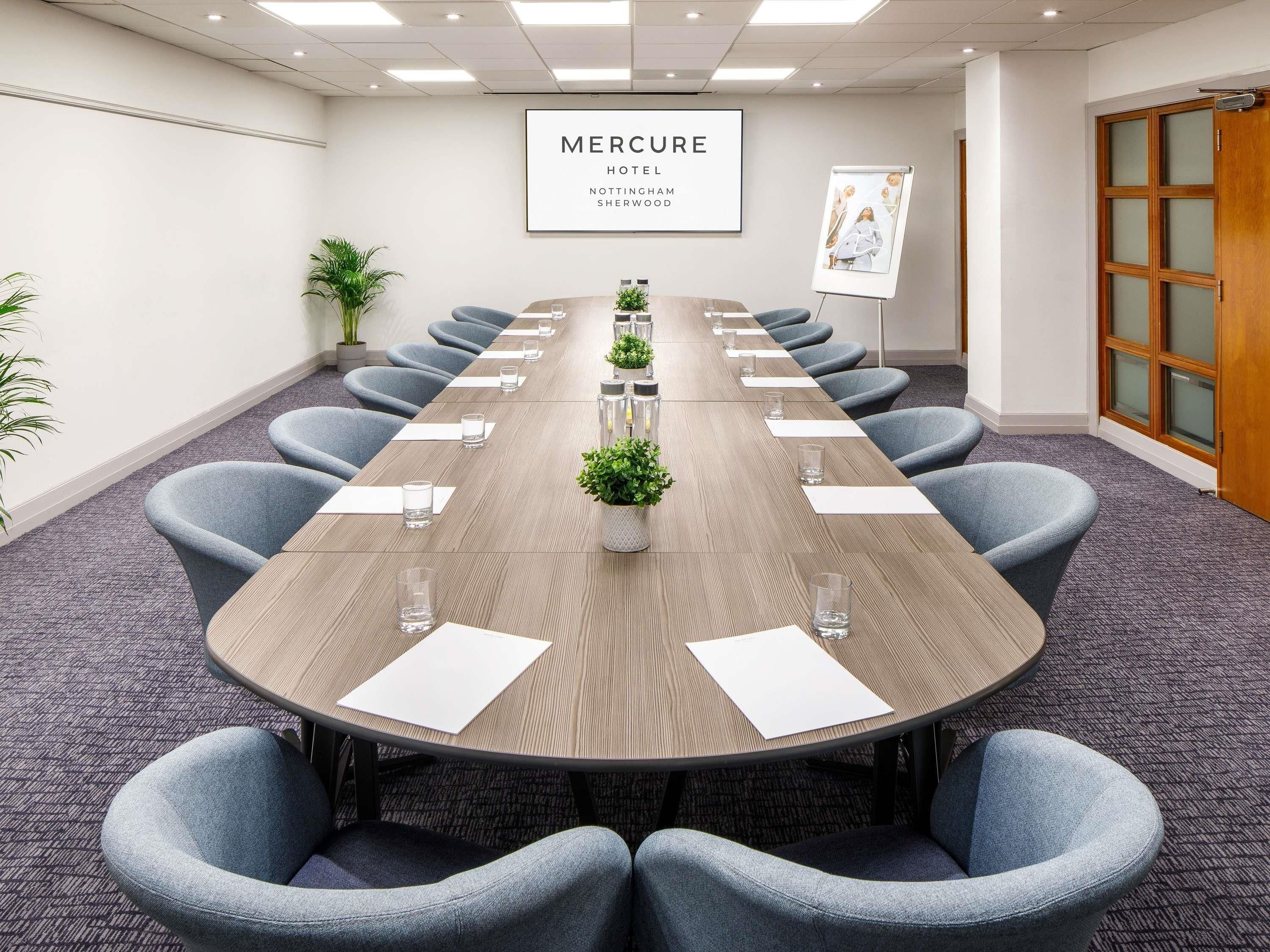 A conference room with a long table, blue chairs, potted plants, and a framed sign on the wall.