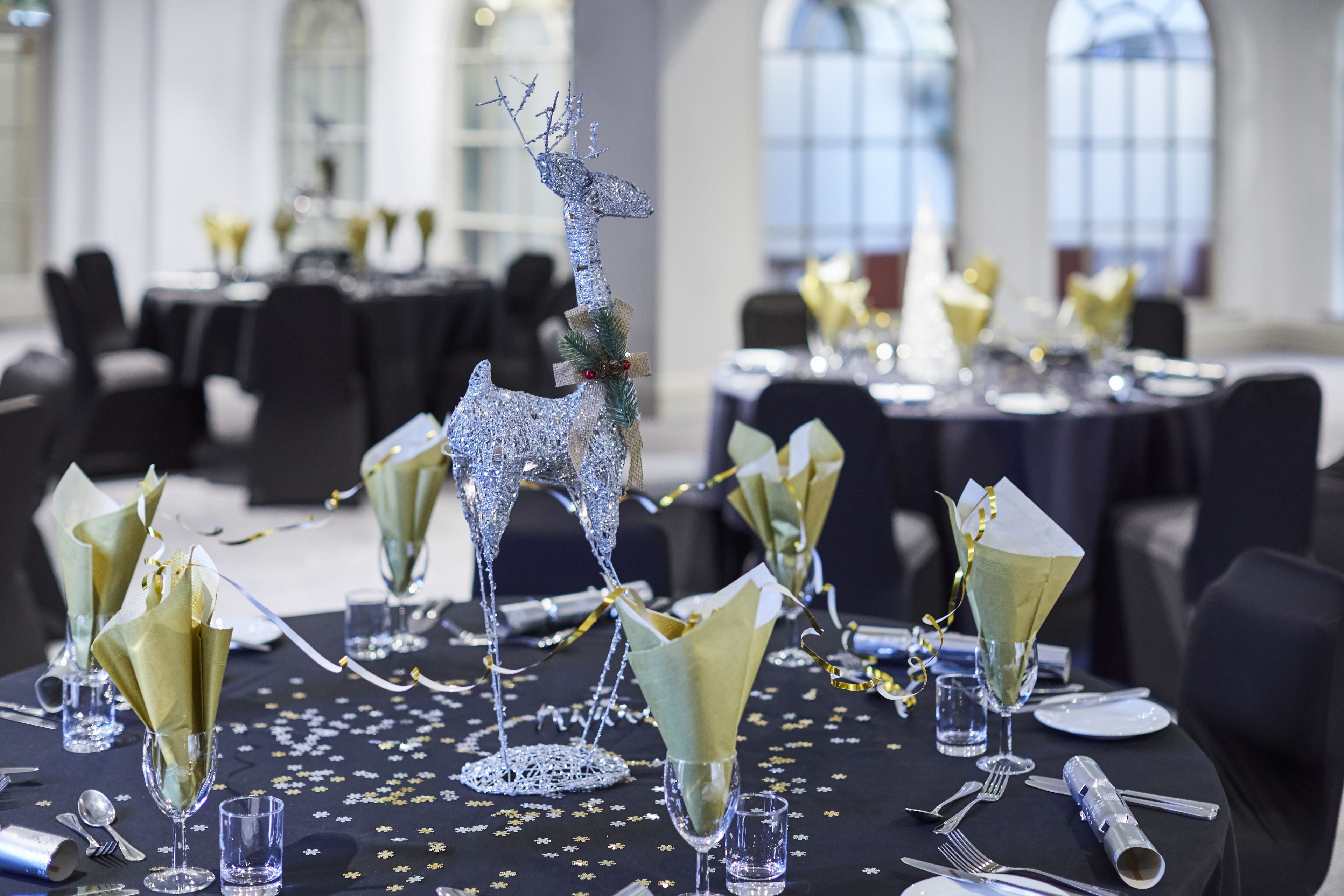 A dining table set with crystal glasses, silverware, and a decorative silver reindeer centerpiece.