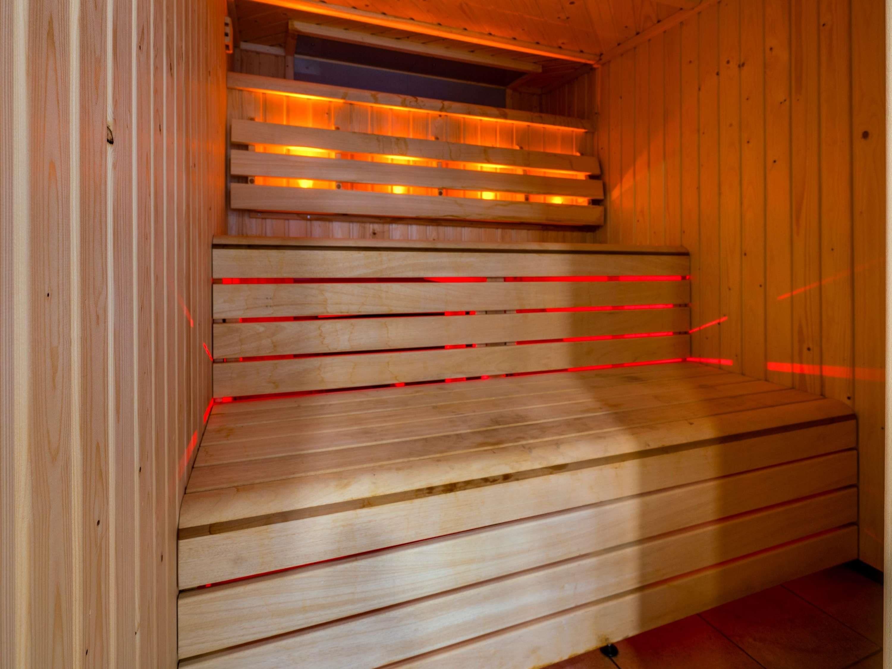 Una sauna de madera con bancos horizontales e iluminación roja.