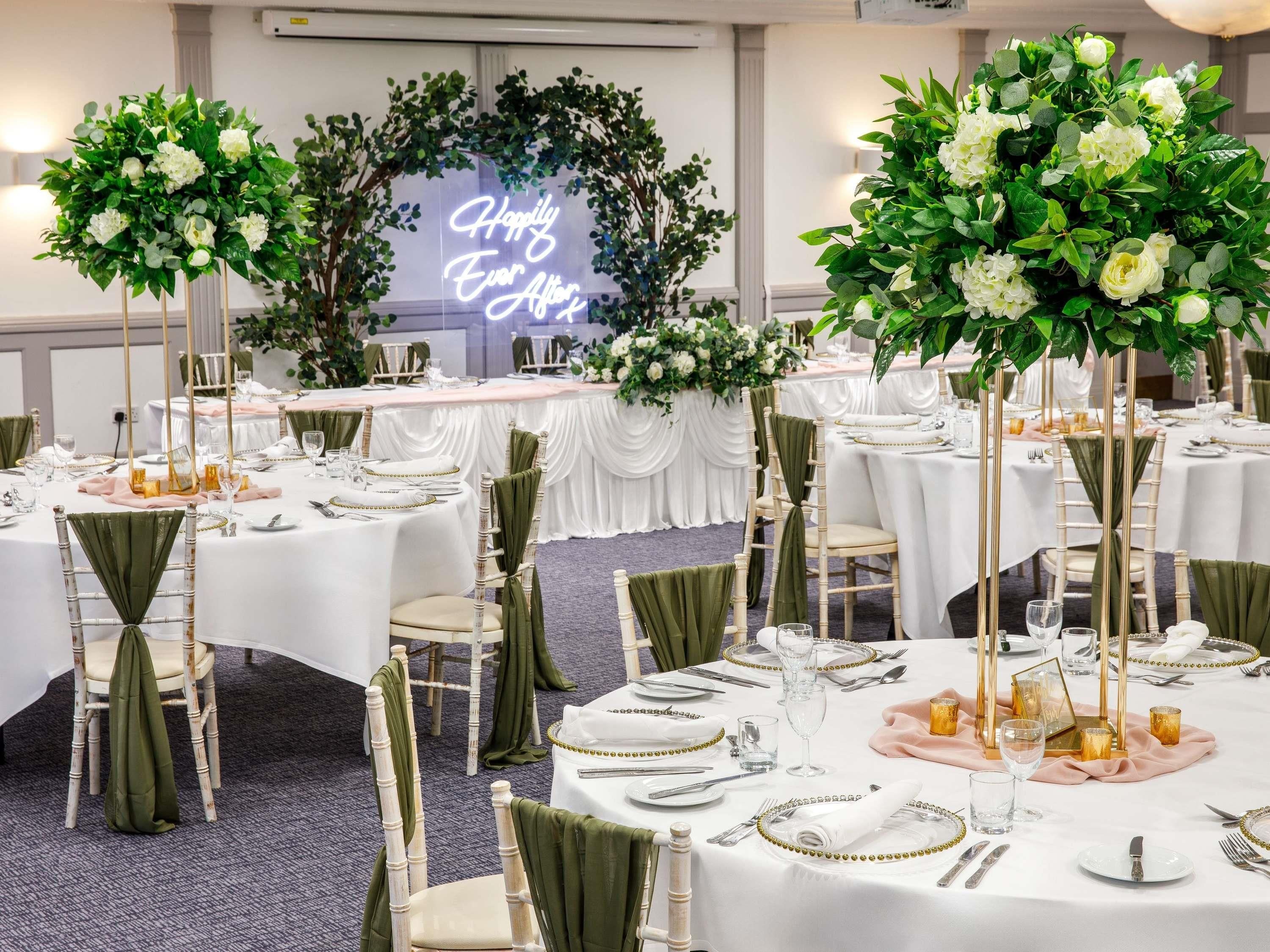 Ein Festsaal mit runden Tischen, grünen Stuhlhussen und floralen Tischdekorationen.
