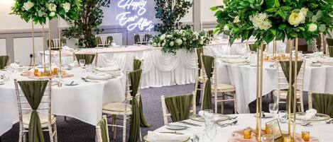 Ein Festsaal mit runden Tischen, grünen Stuhlhussen und floralen Tischdekorationen.