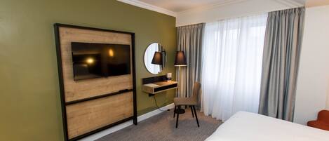 A hotel room with a large bed, a desk with a chair, a TV, and a window with curtains.