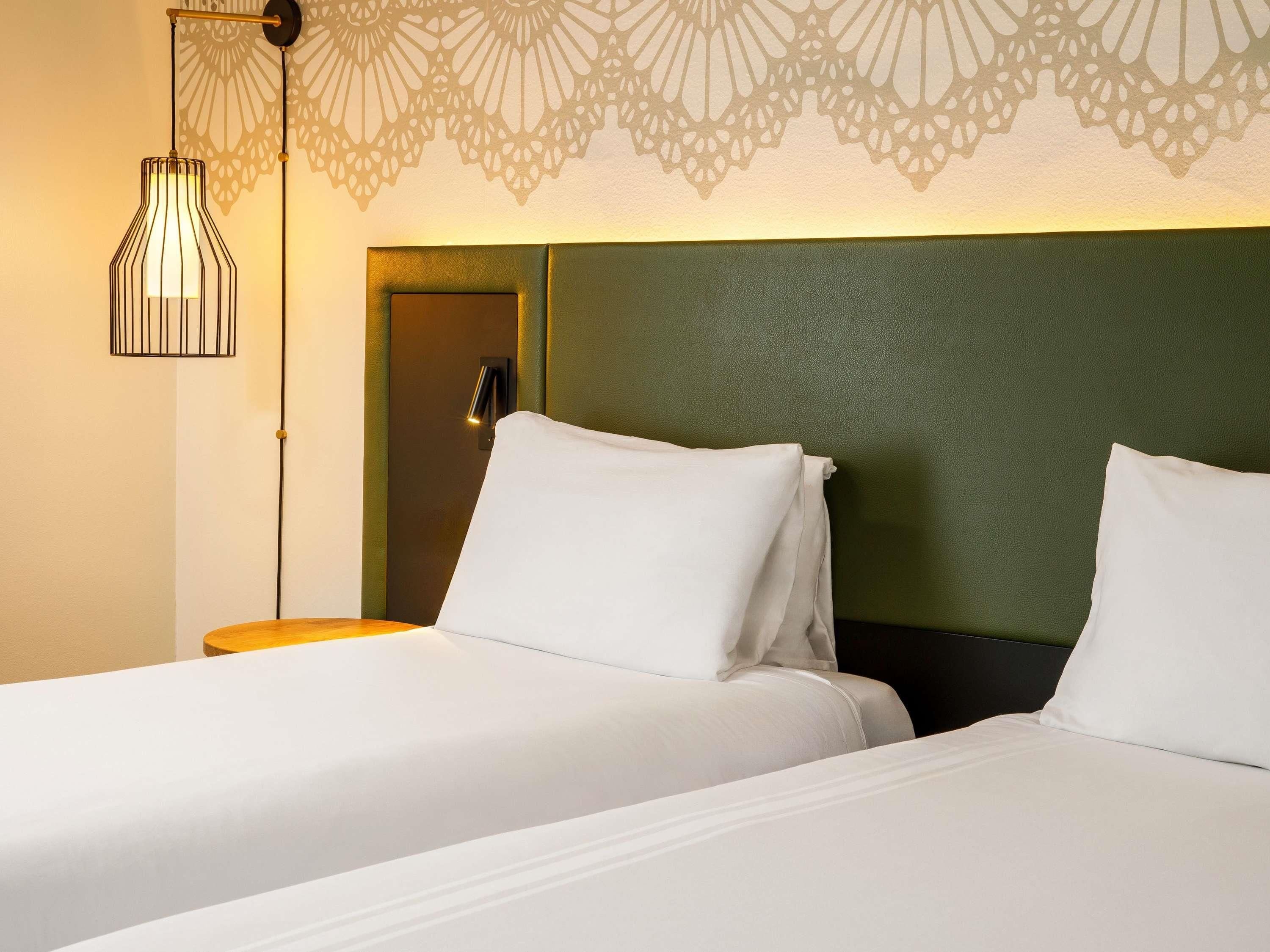 Camera d'albergo con due letti, una lampada a parete e un motivo decorativo sul muro.