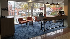 A modern kitchen with a large island, two orange chairs, and a view of the street through large windows. - Mercure Nottingham Sherwood Hotel (Nottingham)
