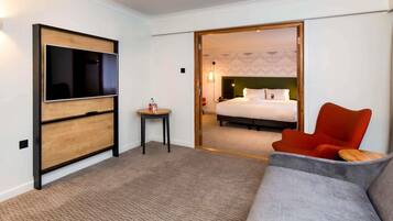 Habitación de hotel con televisor, una mesita con una botella, cama con almohadas y una silla roja.