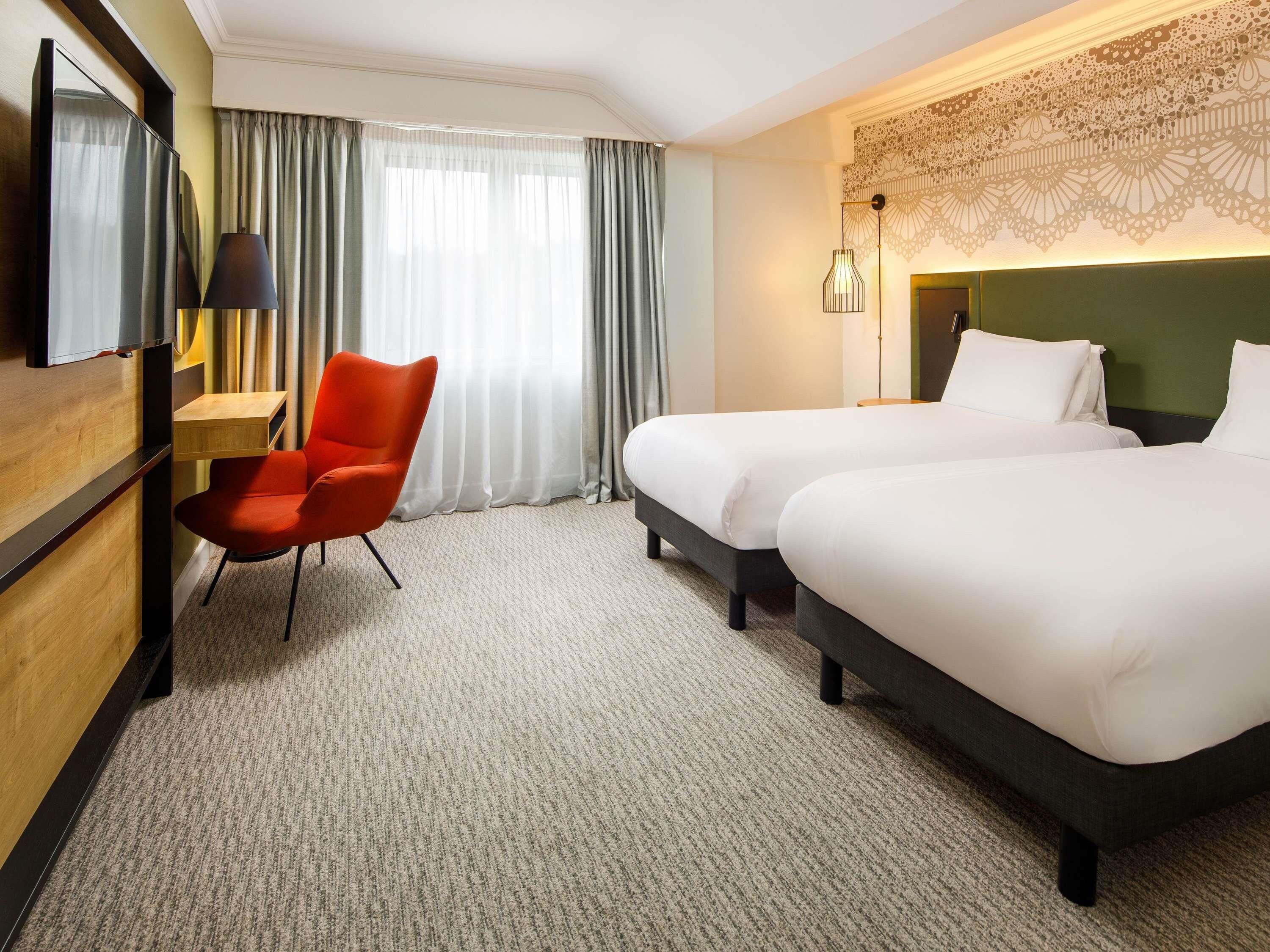 Ett hotellrum med två sängar, ett skrivbord, en stol, en TV och en dekorativ vägg.