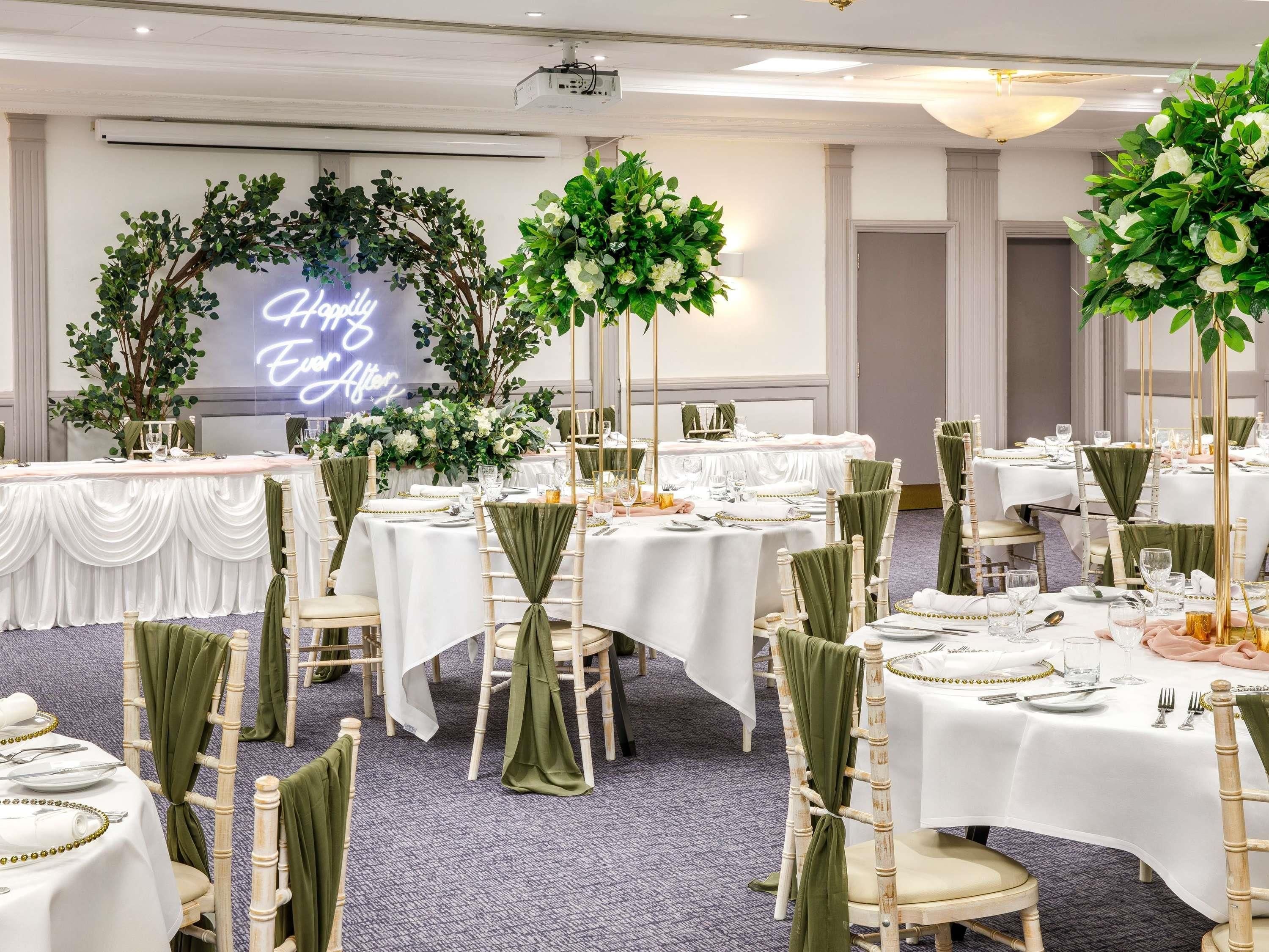 A banquet hall with round tables, green chair sashes, white tablecloths, and floral centerpieces.