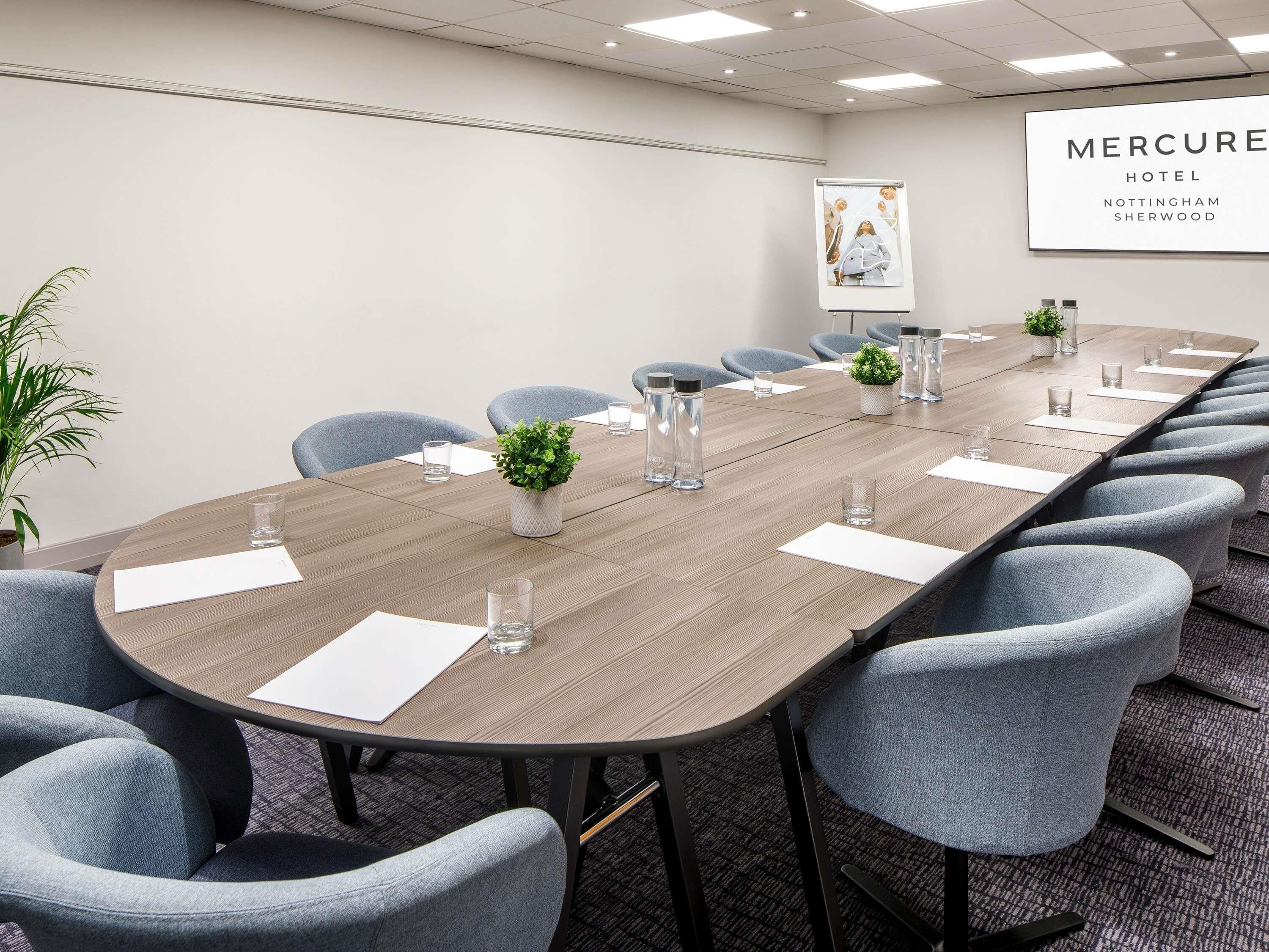 A conference room with a long table, chairs, water bottles, and a potted plant.