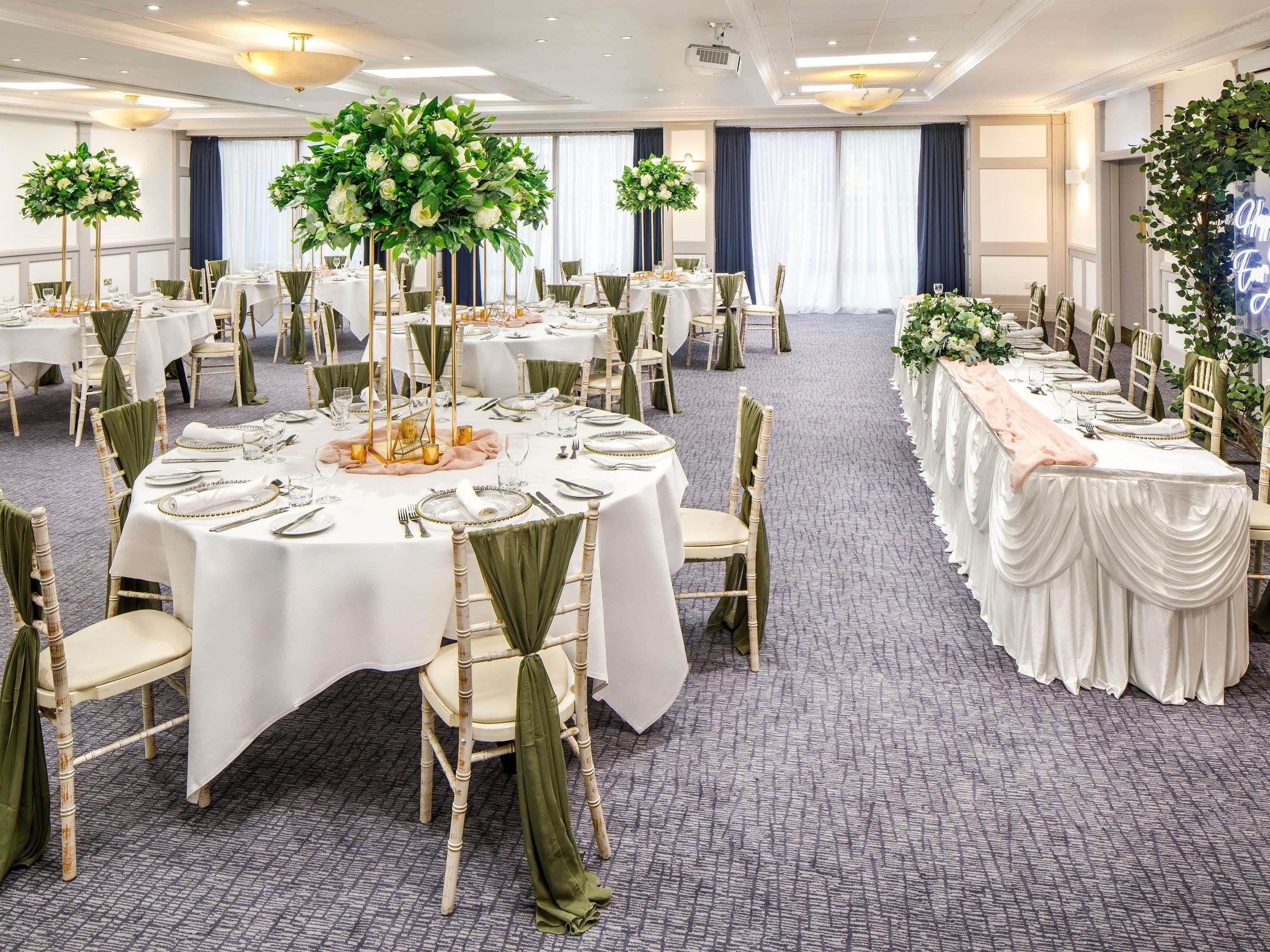 Un salón de banquetes con mesas redondas, sillas verdes y manteles blancos.