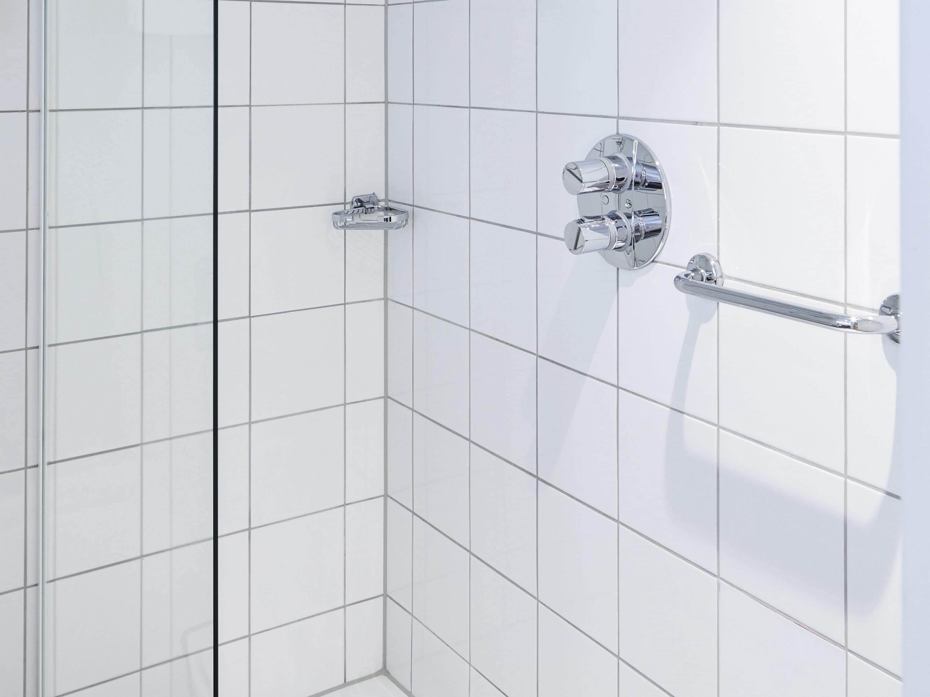 A tiled shower area with a chrome shower head and control knobs.