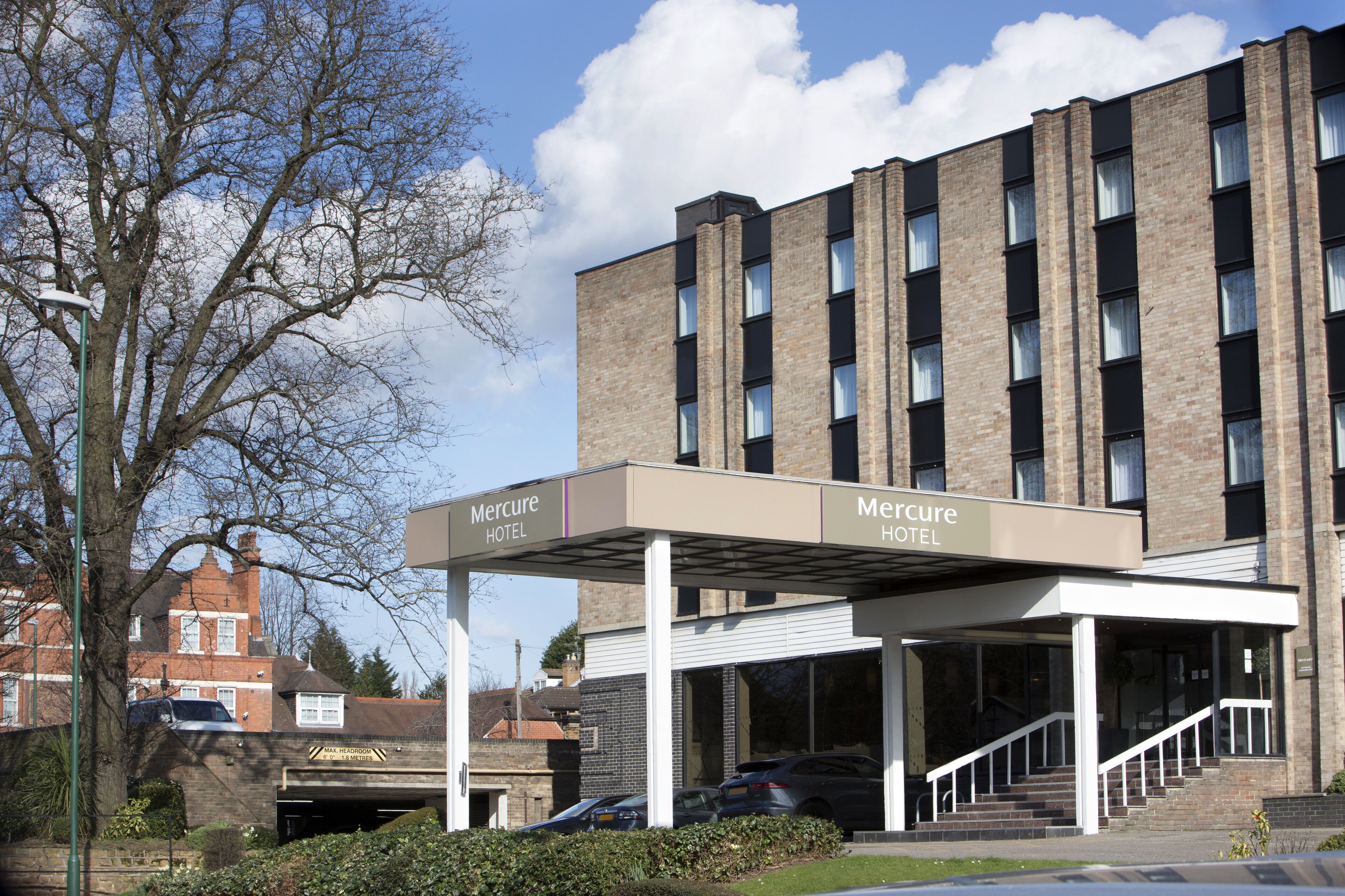 A Mercure hotel with a covered entrance, brick facade, and a parking area with cars.