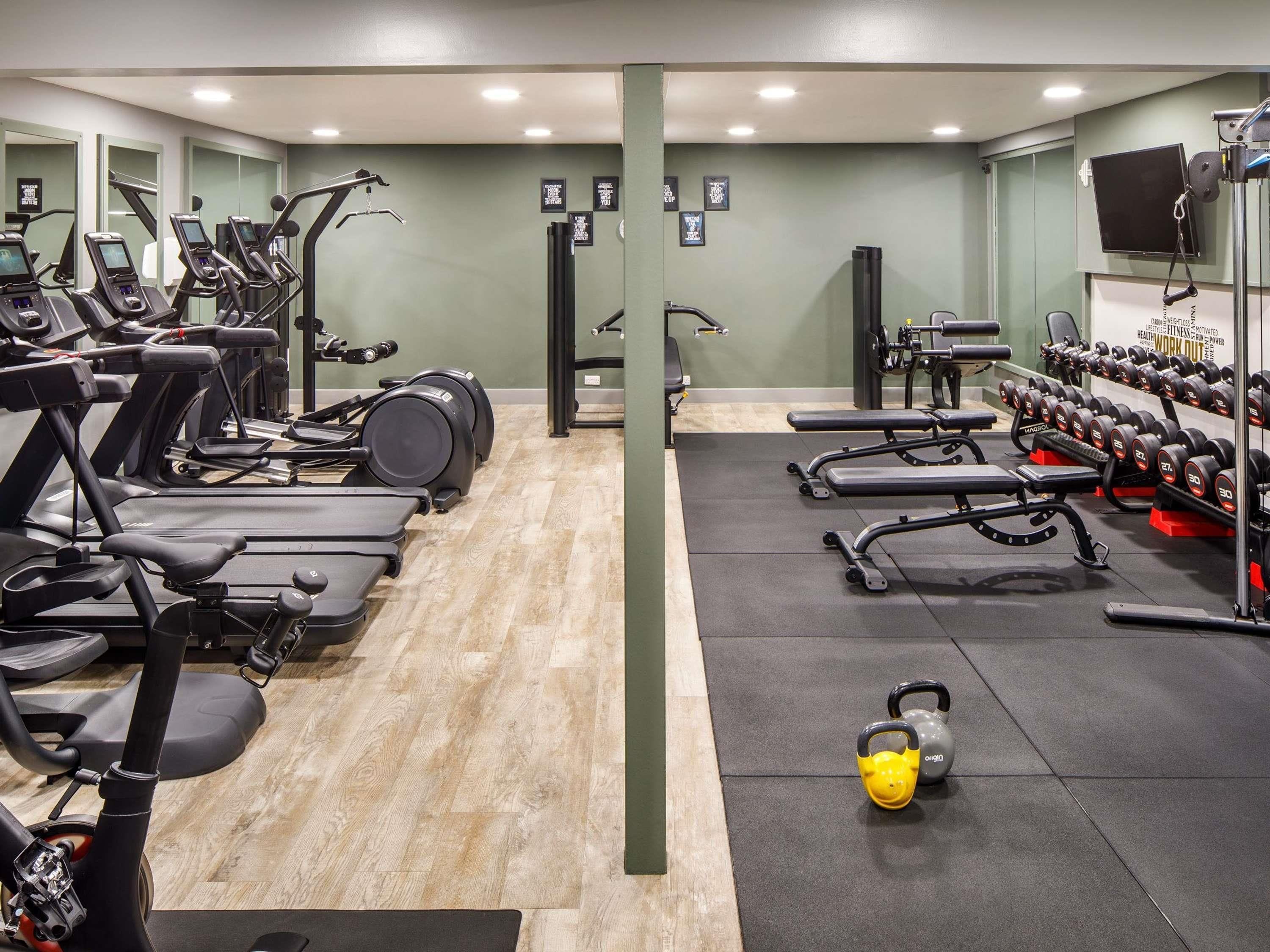A gym with treadmills, elliptical machines, weight benches, and kettlebells.