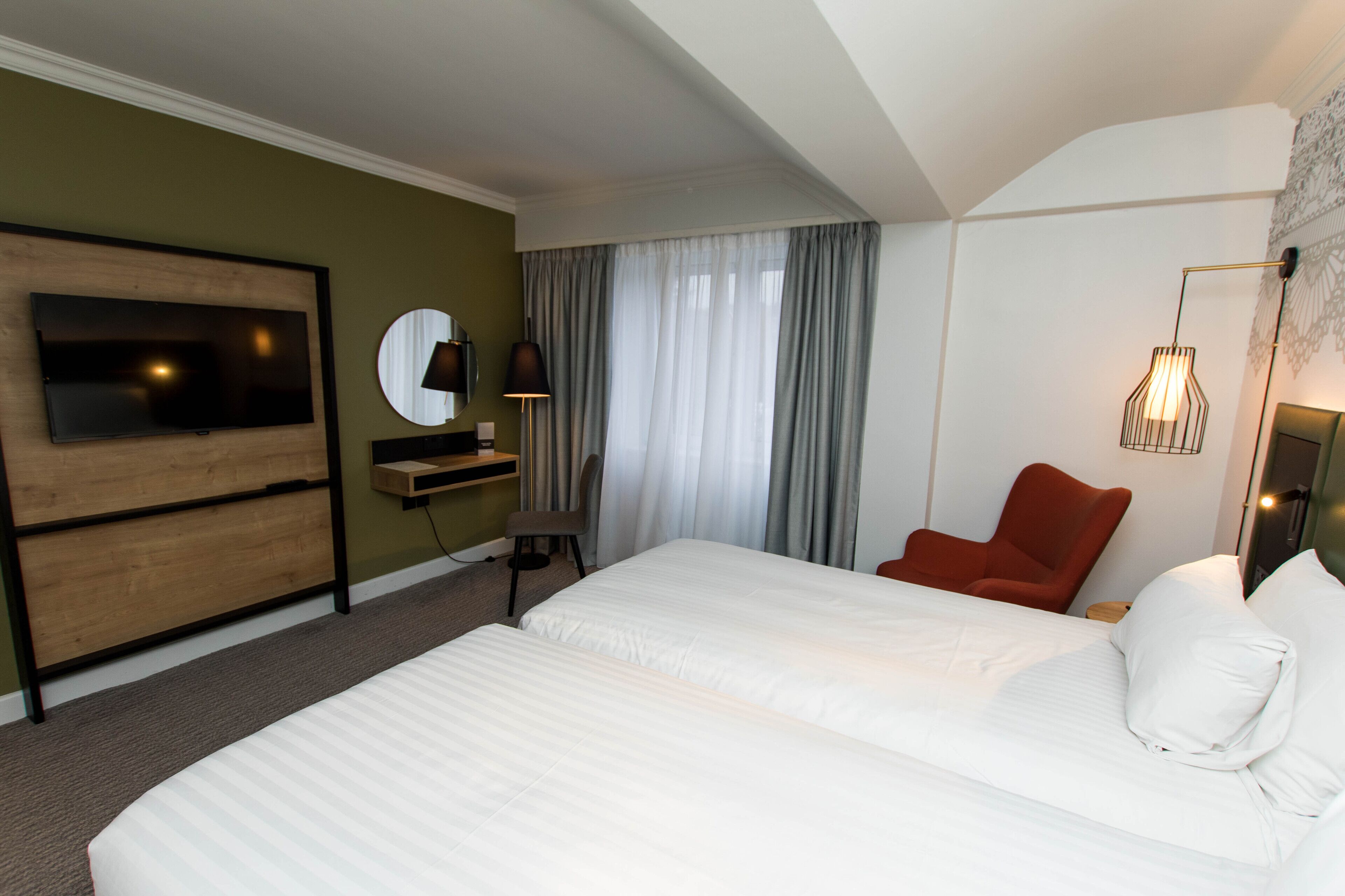 Habitación de hotel con una cama grande, televisor montado en la pared, escritorio con silla y sillón rojo.
