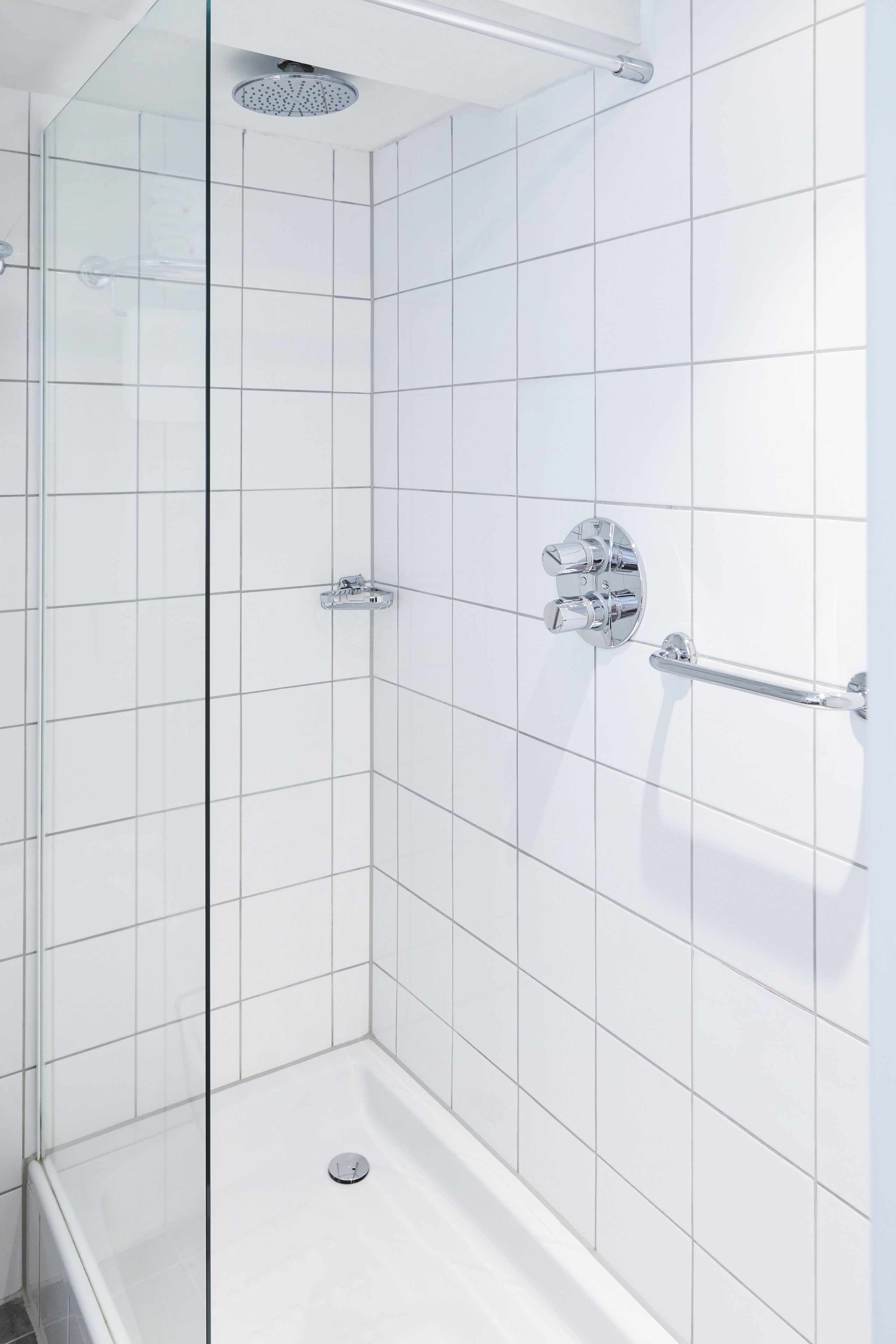 Eine moderne Dusche mit Glastür, Chromarmaturen und Fliesenboden.
