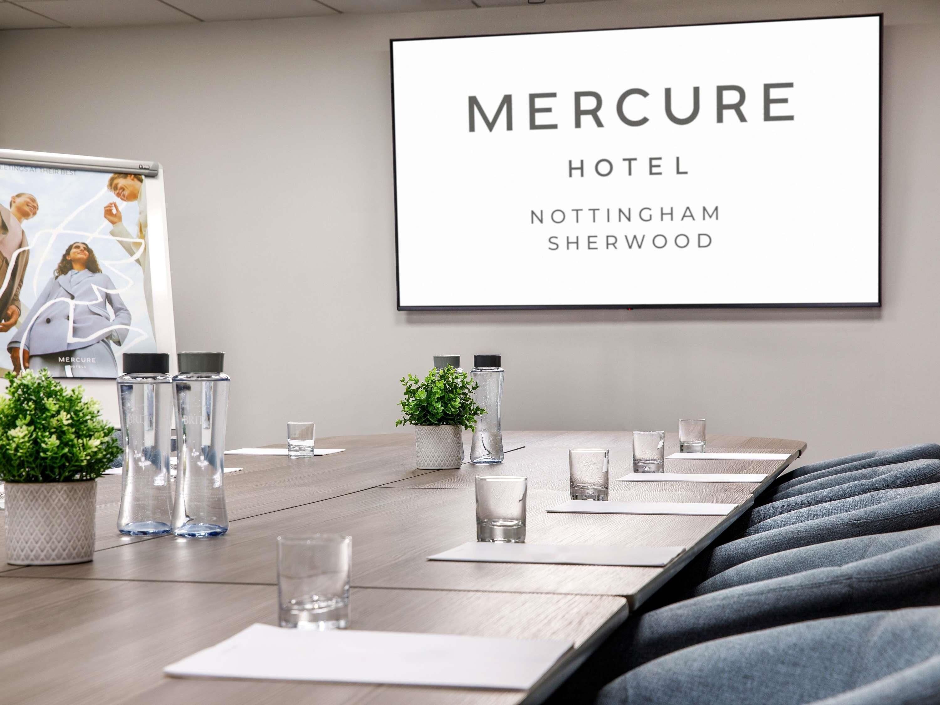 A conference room with a long table, chairs, water bottles, glasses, and a framed sign for Mercure Hotel Nottingham Sherwood.