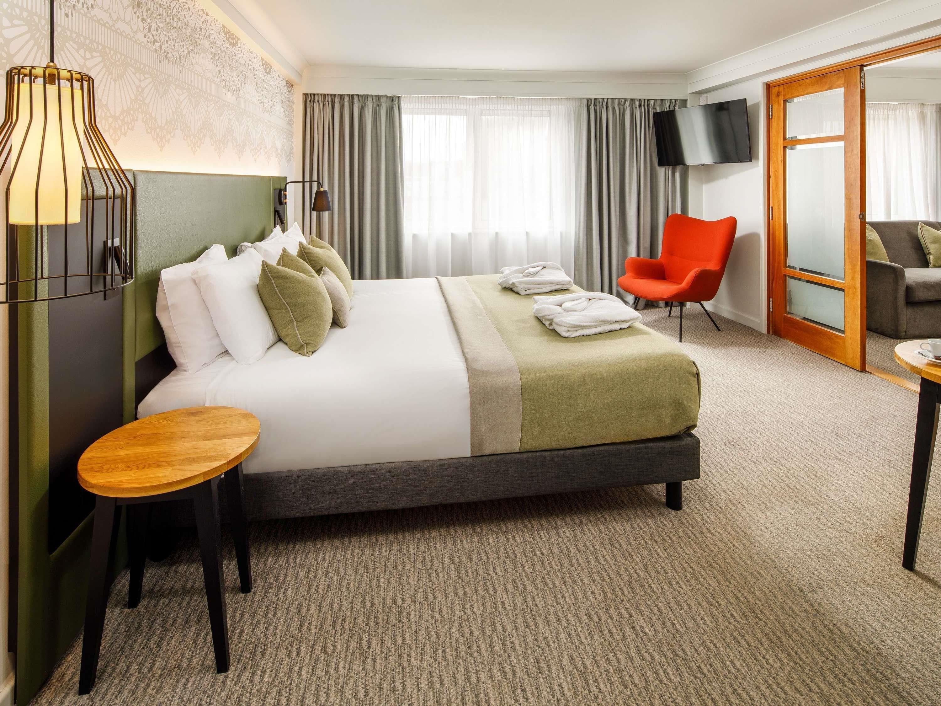 Una habitación de hotel con una cama grande, un escritorio, una silla, un televisor y una puerta corrediza.