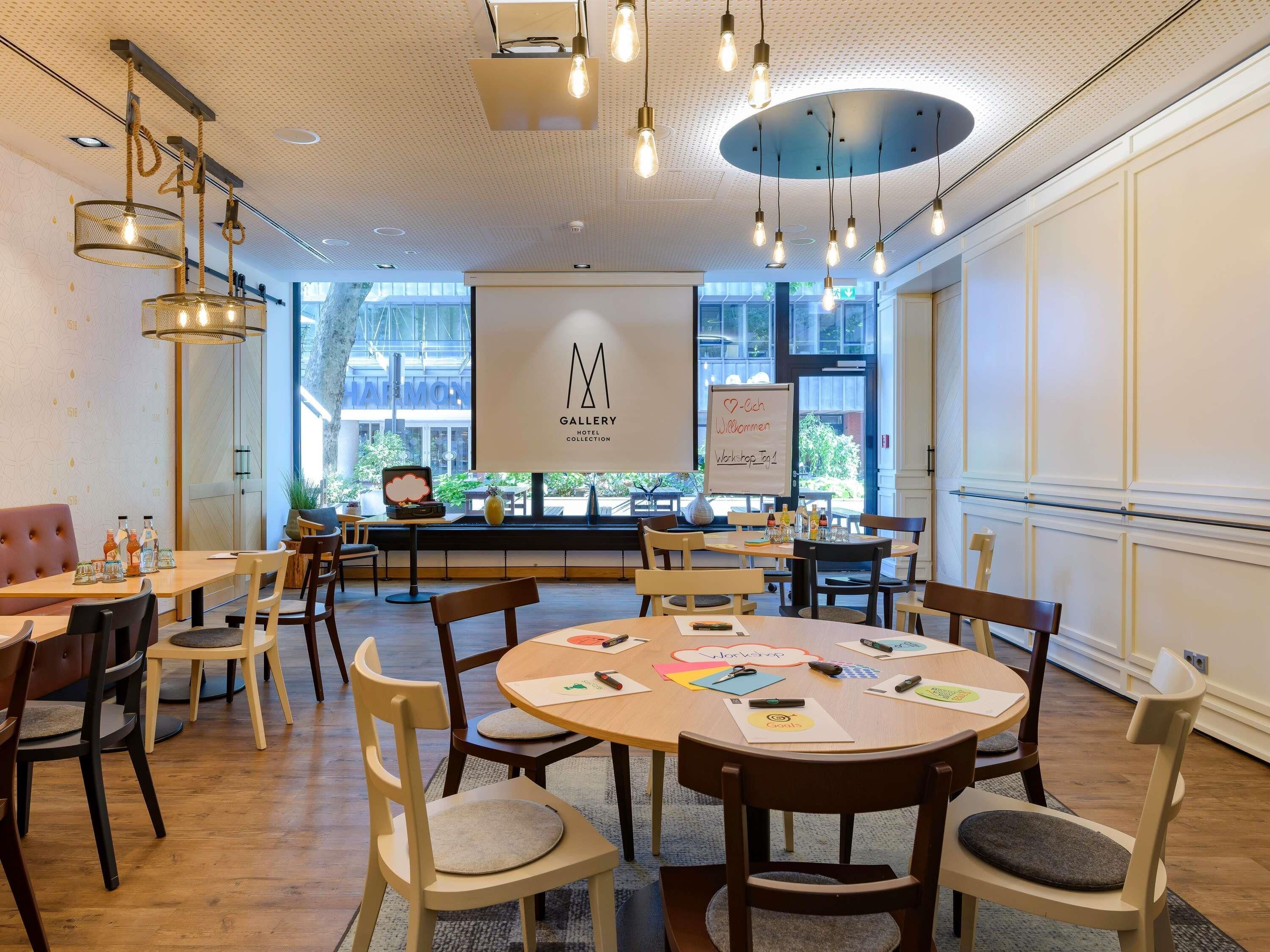A modern hotel lobby with round tables, comfortable seating, a large whiteboard, and a view of the outside.