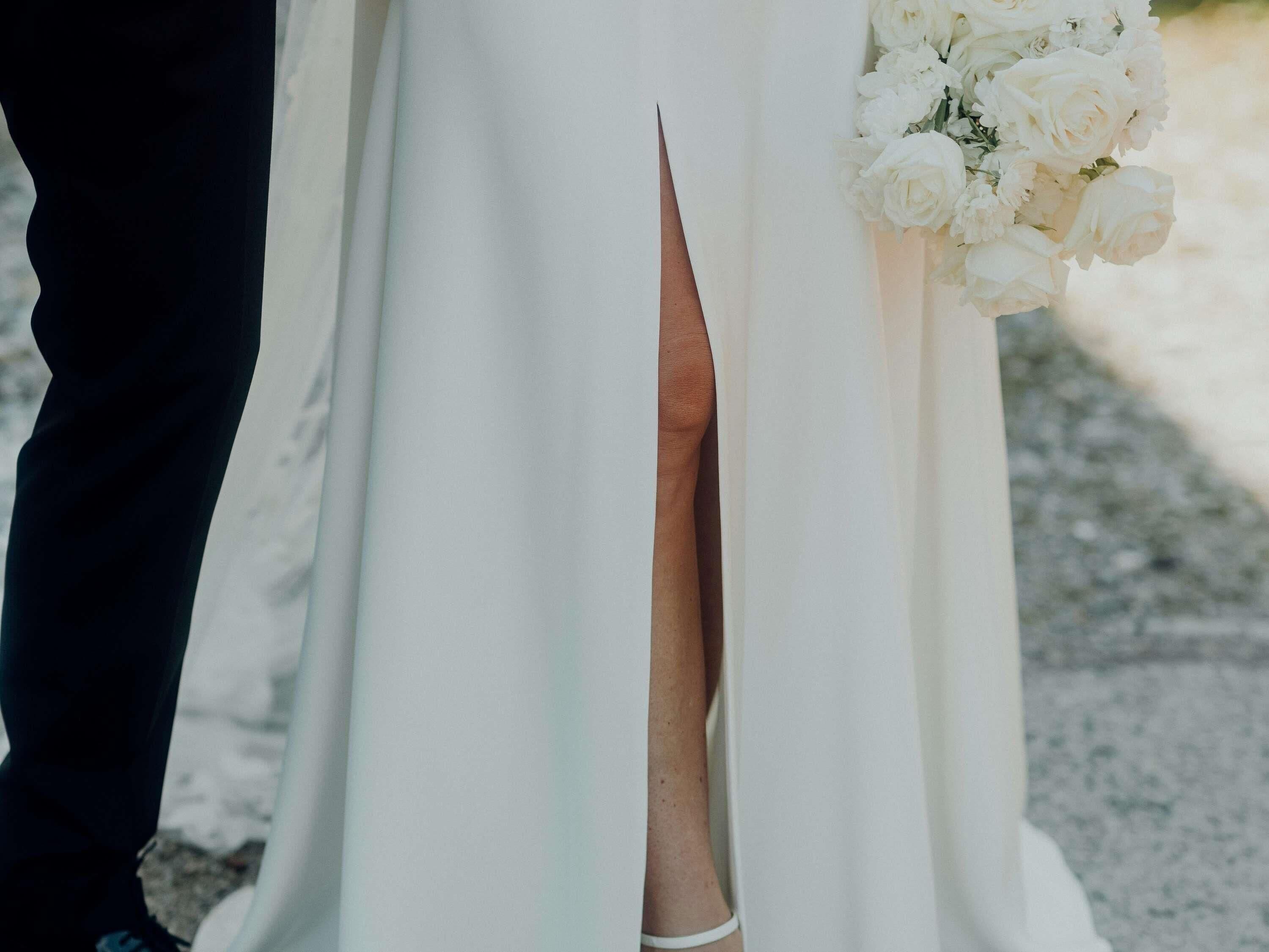 A wedding dress with a slit detail and a bouquet of white flowers.