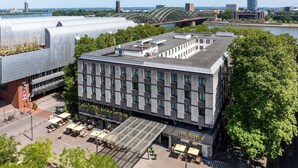 A modern building with a flat roof, large windows, and outdoor seating area. - Hotel Mondial am Dom Cologne - MGallery (Cologne)