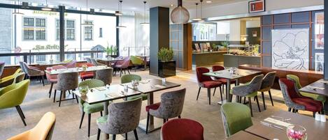 Un restaurante moderno con varias mesas y sillas, ventanas amplias y plantas de interior.