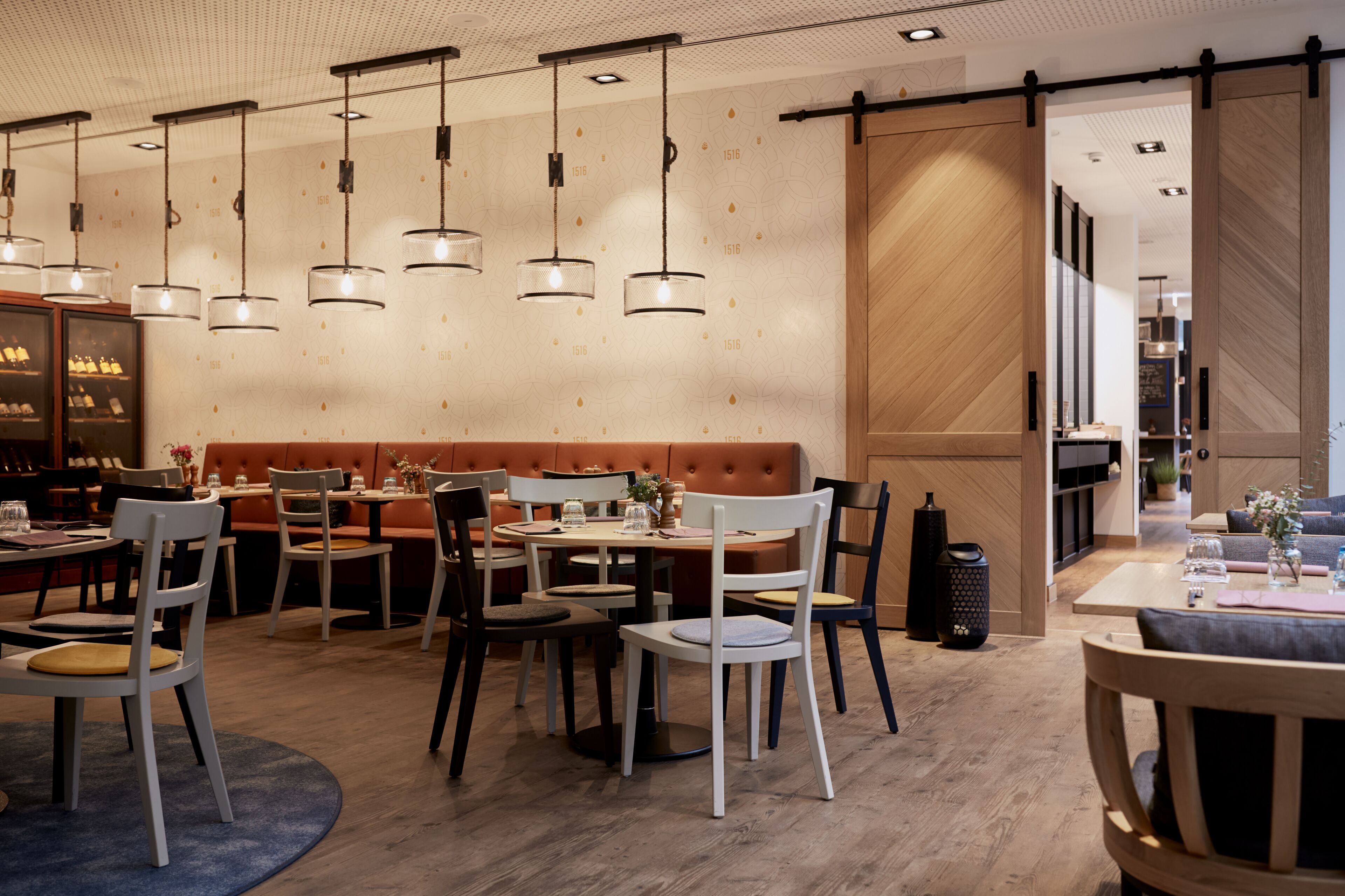 Un restaurante moderno con varias zonas de comedor, incluyendo una zona con asientos tipo cabina y mesas individuales.