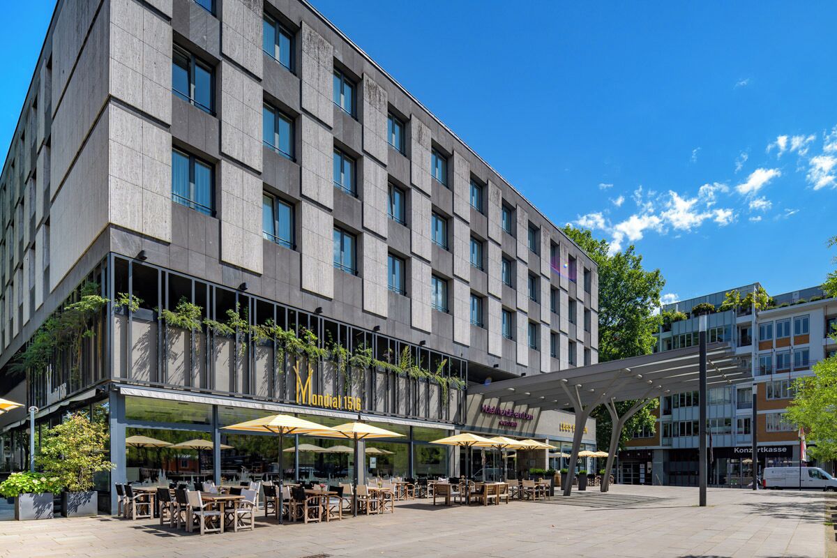 Un hotel moderno con mesas al aire libre, un porche cubierto y un cielo despejado.