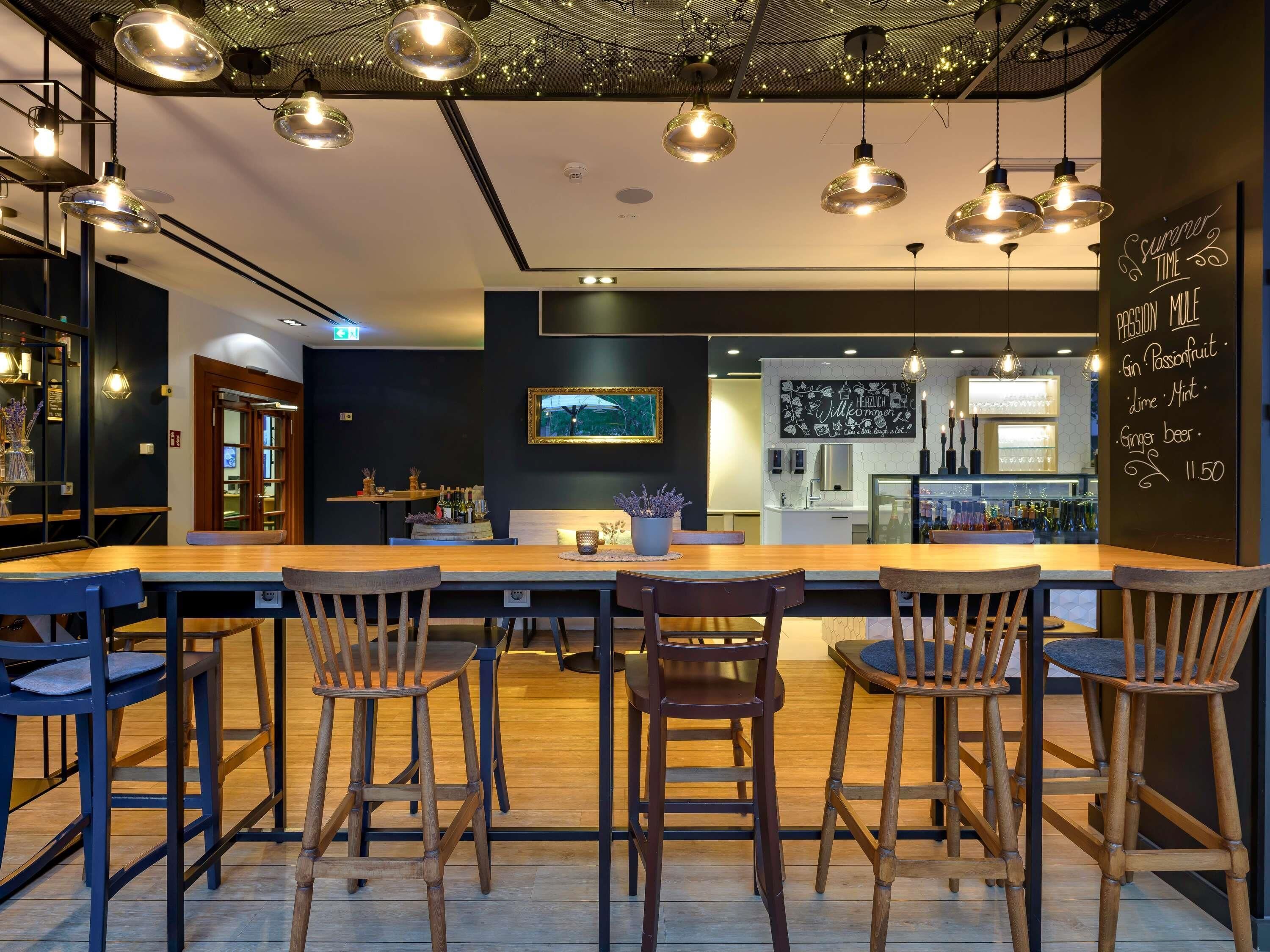 A modern bar area with wooden tables and chairs, pendant lighting, and a chalkboard menu.