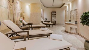 A spa room with reclining chairs, a massage table, a wall mural, a fireplace, and a potted plant. - Hotel Mondial am Dom Cologne - MGallery (Cologne)