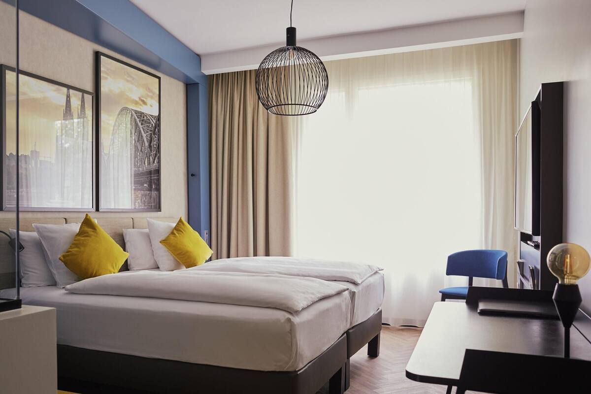 A modern hotel room with a large bed, a desk, a chair, and a cityscape view.