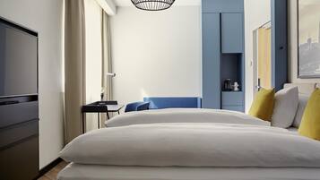 A hotel room with a bed, a desk, a chair, a television, a wardrobe, and a hanging light fixture.