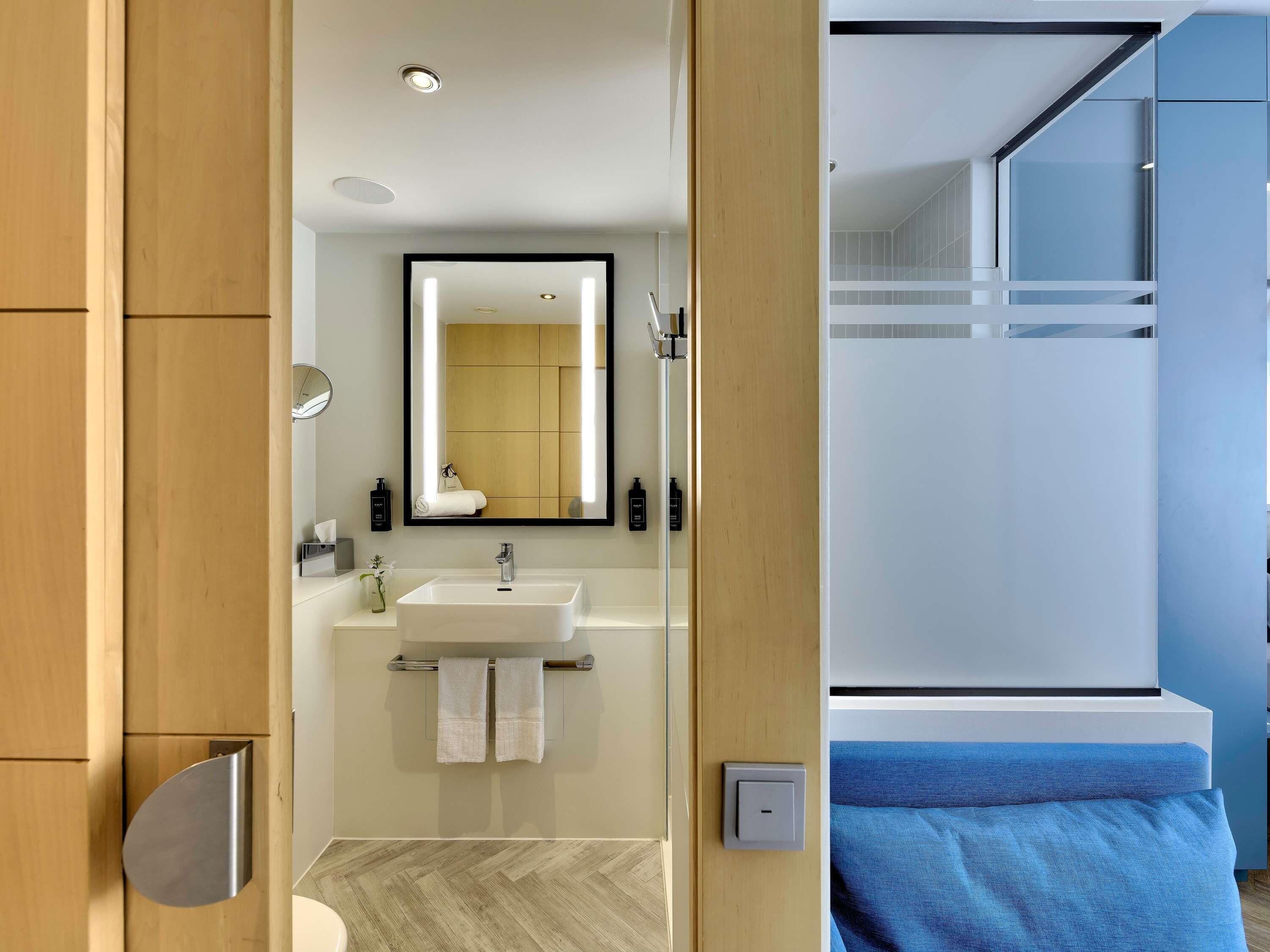 A modern bathroom with a wooden vanity, a large mirror, a white sink, and a towel rack.