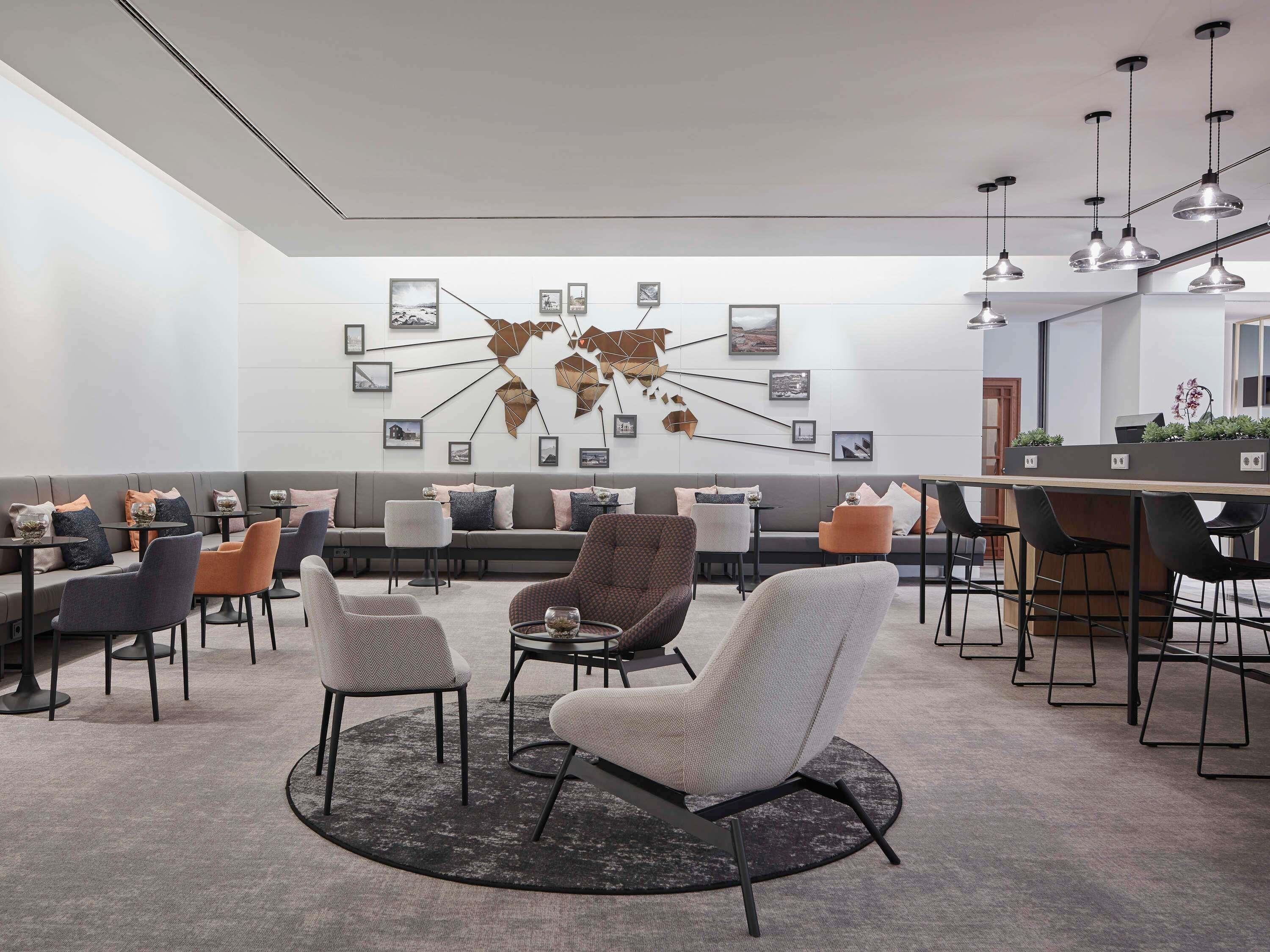 A modern lounge with a sofa, chairs, a coffee bar, and a world map wall art.