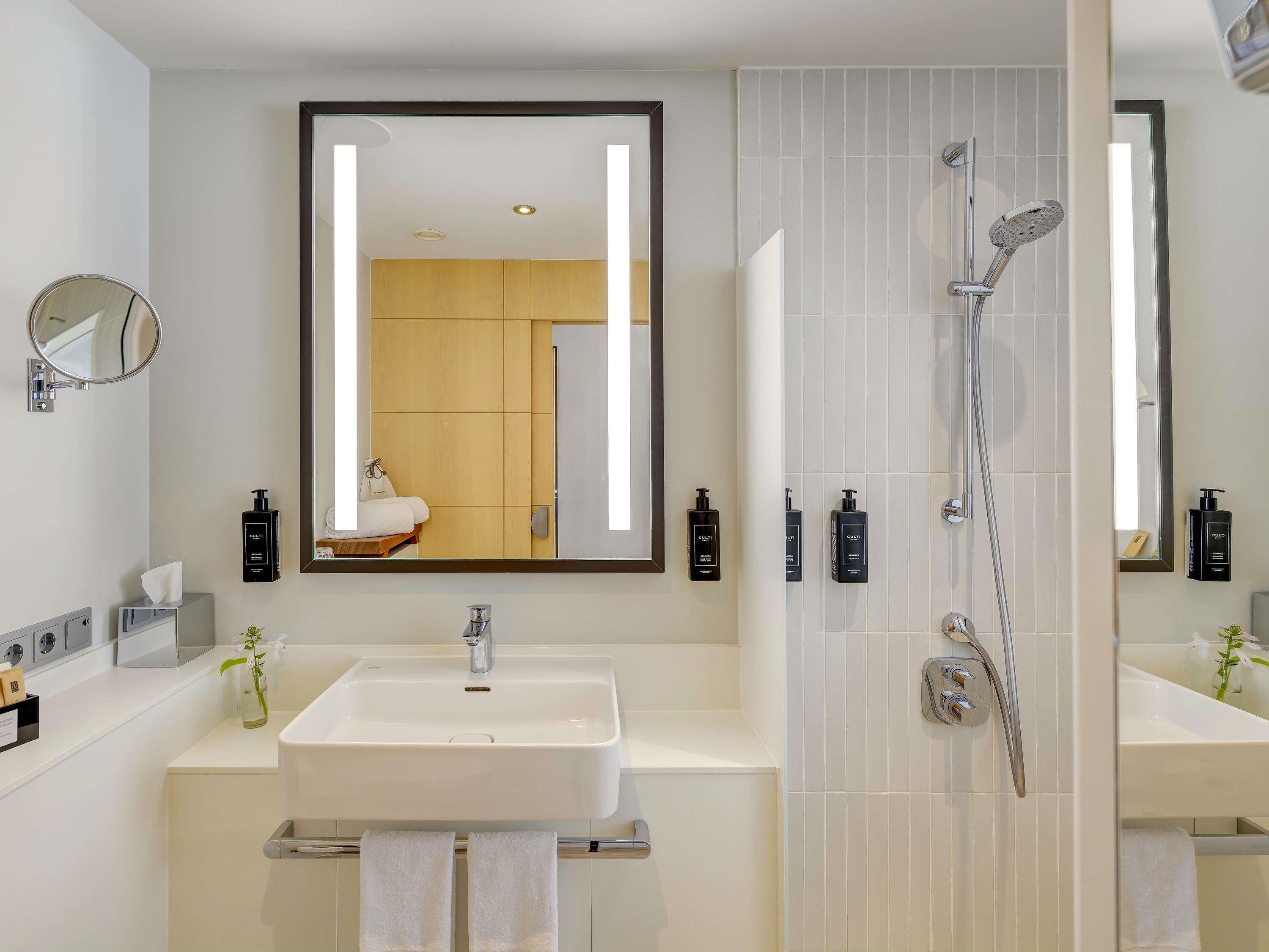 A modern bathroom with a large mirror, a sink, a shower, and toiletries.