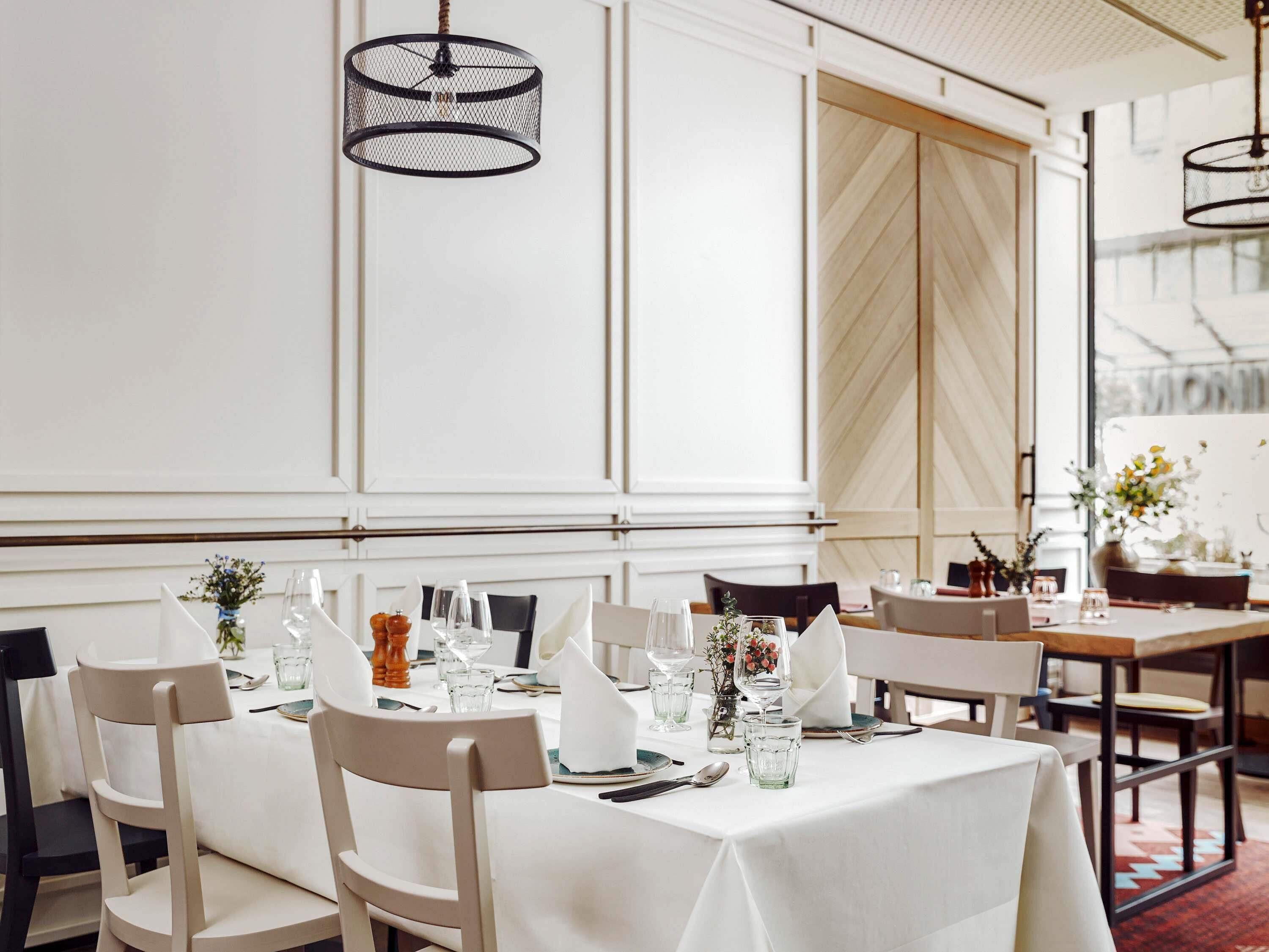 A restaurant with white tablecloths, black mesh pendant lights, and a herringbone wood panel wall.