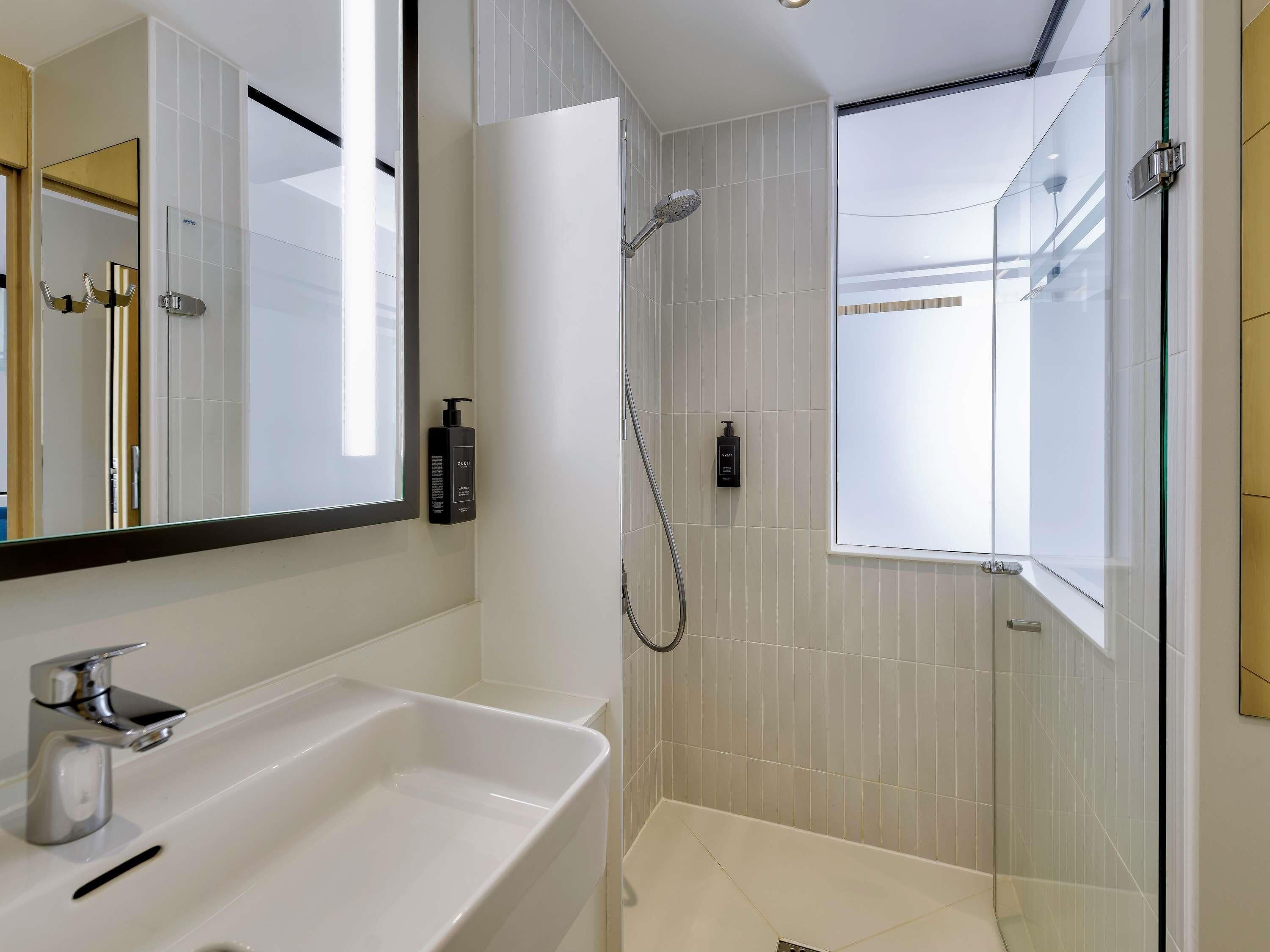 Un baño moderno con un espejo grande, un lavabo, una ducha y dos botellas de champú.