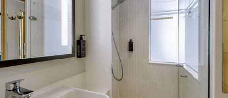 Un baño moderno con un espejo grande, un lavabo, una ducha y dos botellas de champú.