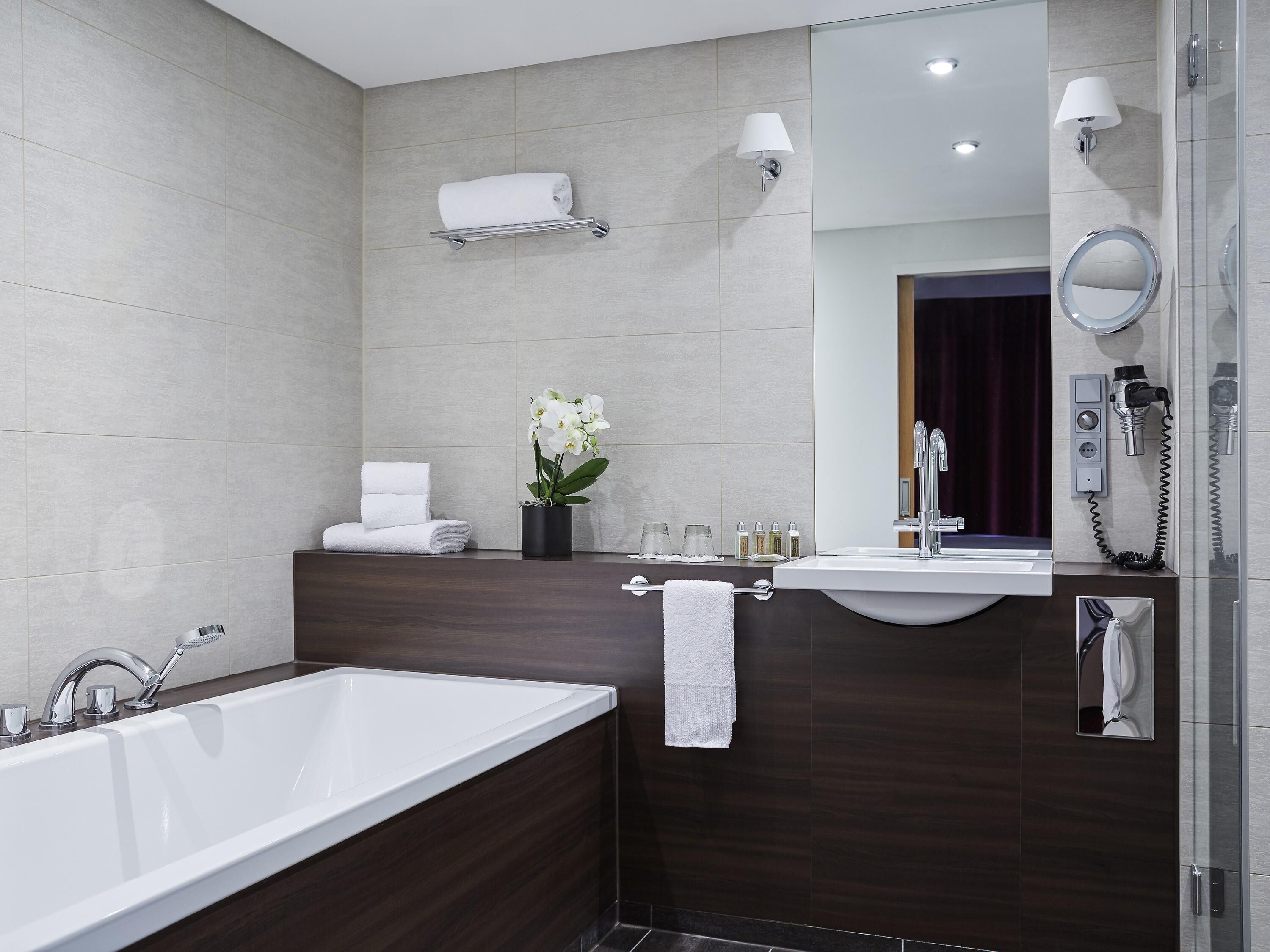 A modern bathroom with a bathtub, a vanity with a mirror, a towel rack, and a wall-mounted phone.