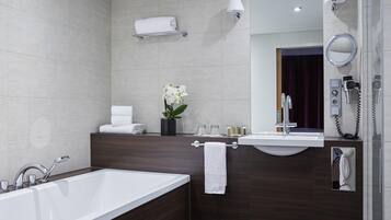 A modern bathroom with a bathtub, a vanity with a mirror, a towel rack, and a wall-mounted phone.